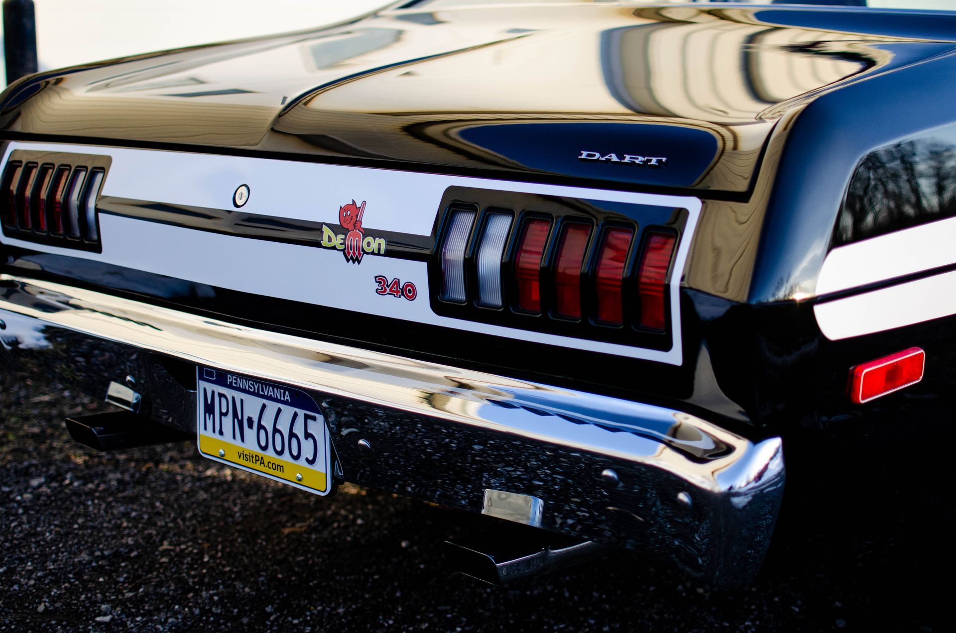 Rear view of a black classic Ford Mustang with chrome bumper and red taillights parked on a street.