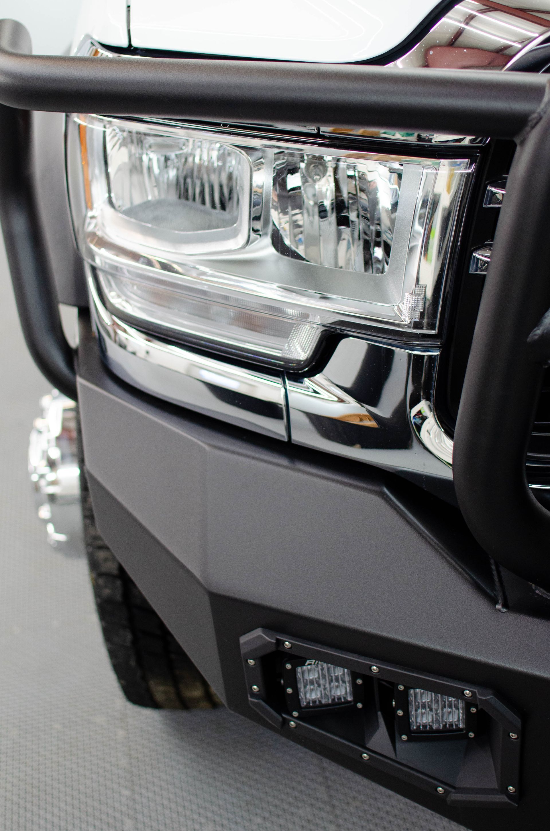 Close-up of a rugged vehicle front headlight and bumper with a black protective grille.
