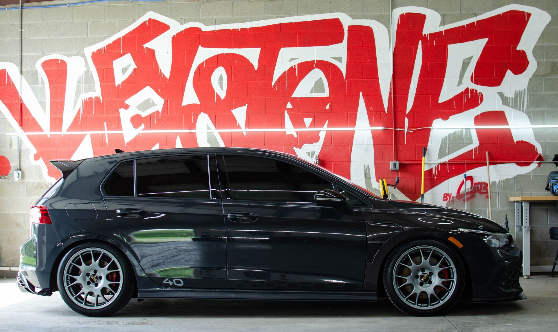 Black sports coupe parked indoors in front of a red graffiti wall