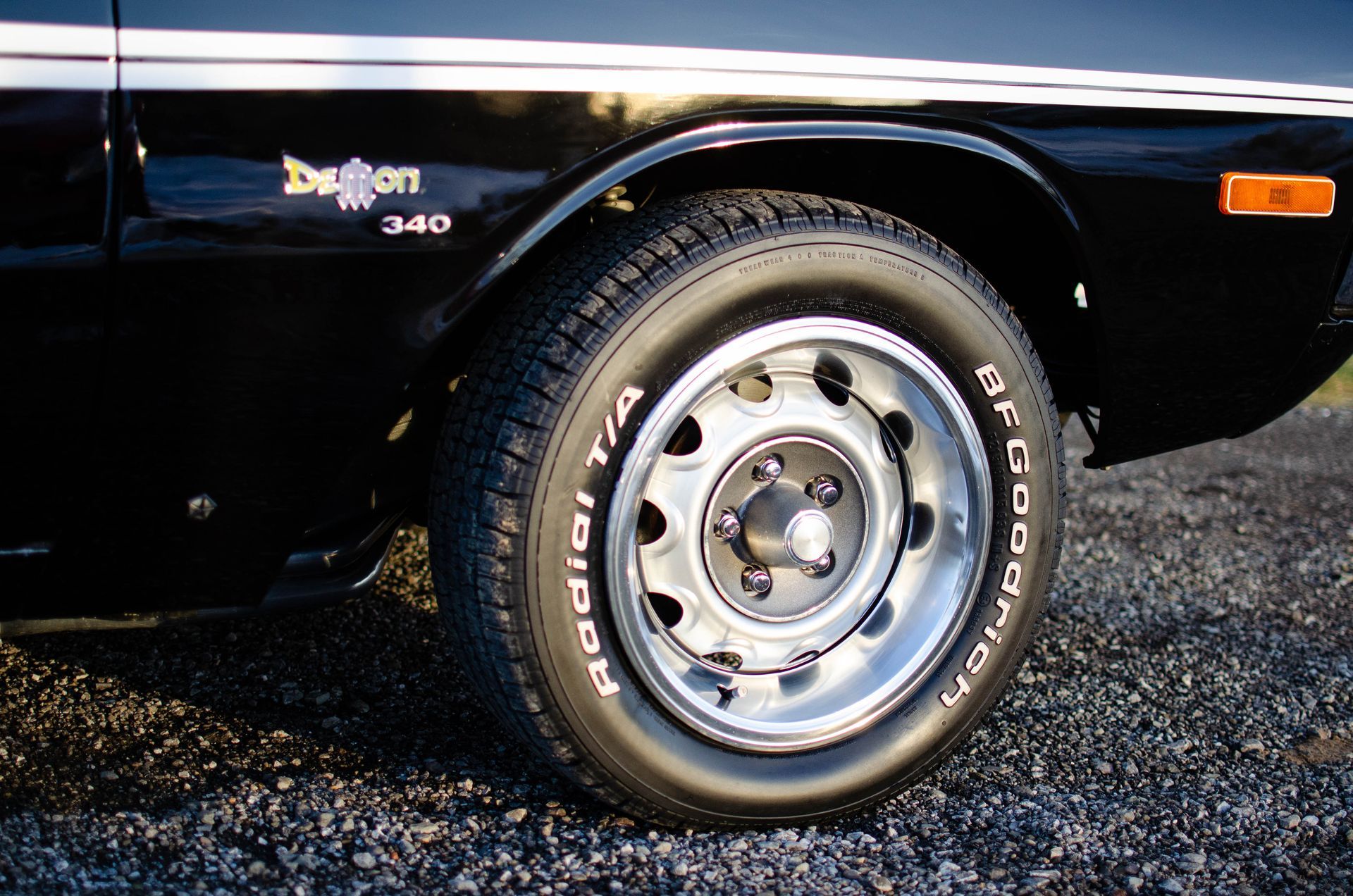 Close-up of a black car’s front wheel and tire on gravel