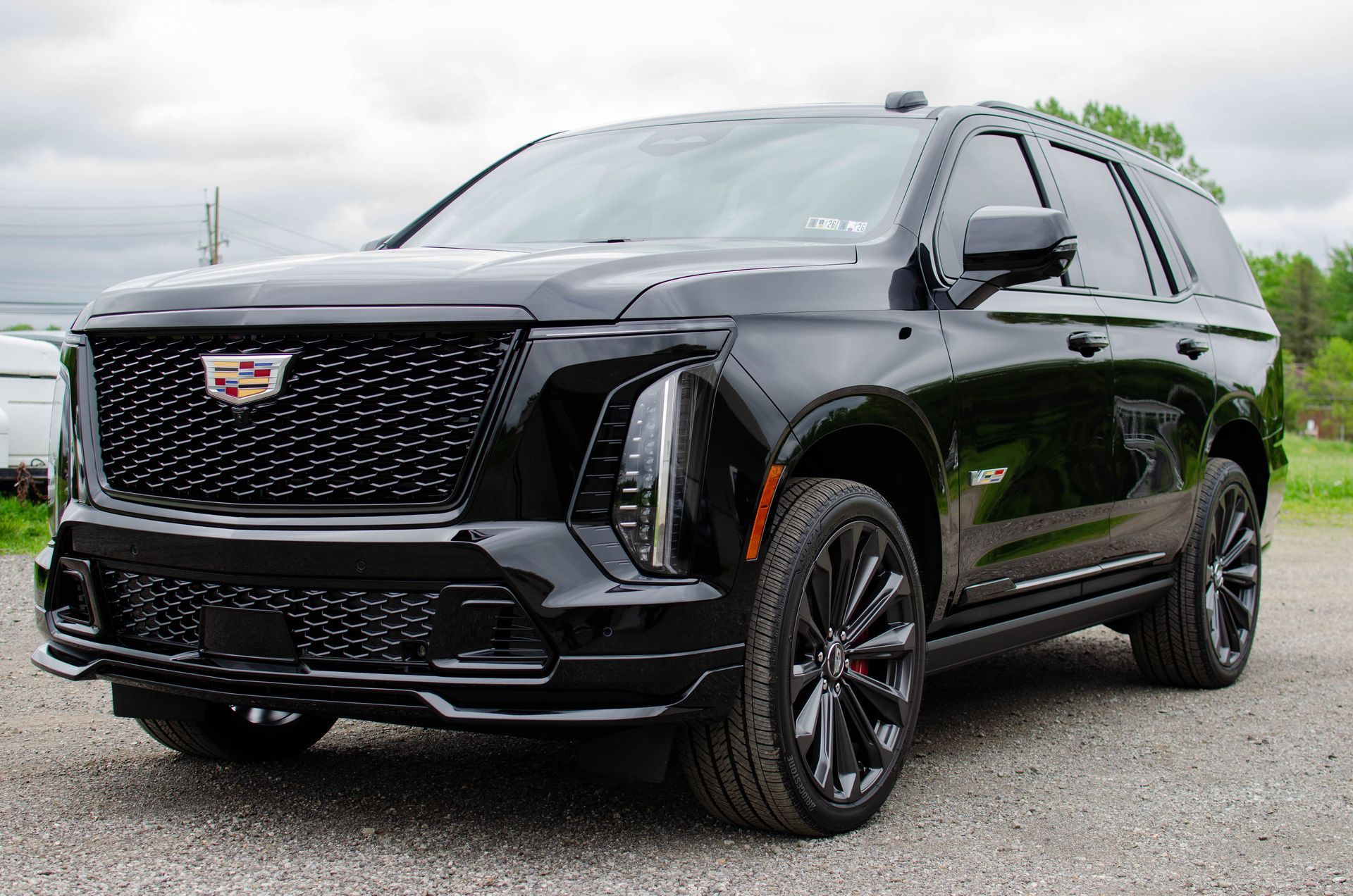 Black Cadillac Escalade parked outdoors on a gravel lot under cloudy skies