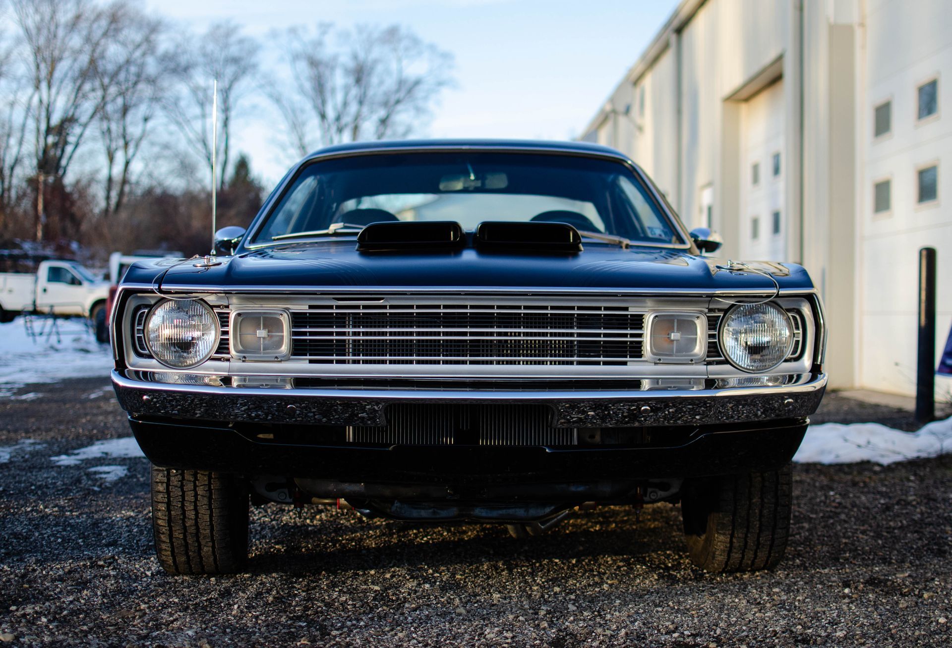 Front view of a black classic muscle car parked on gravel beside a building.