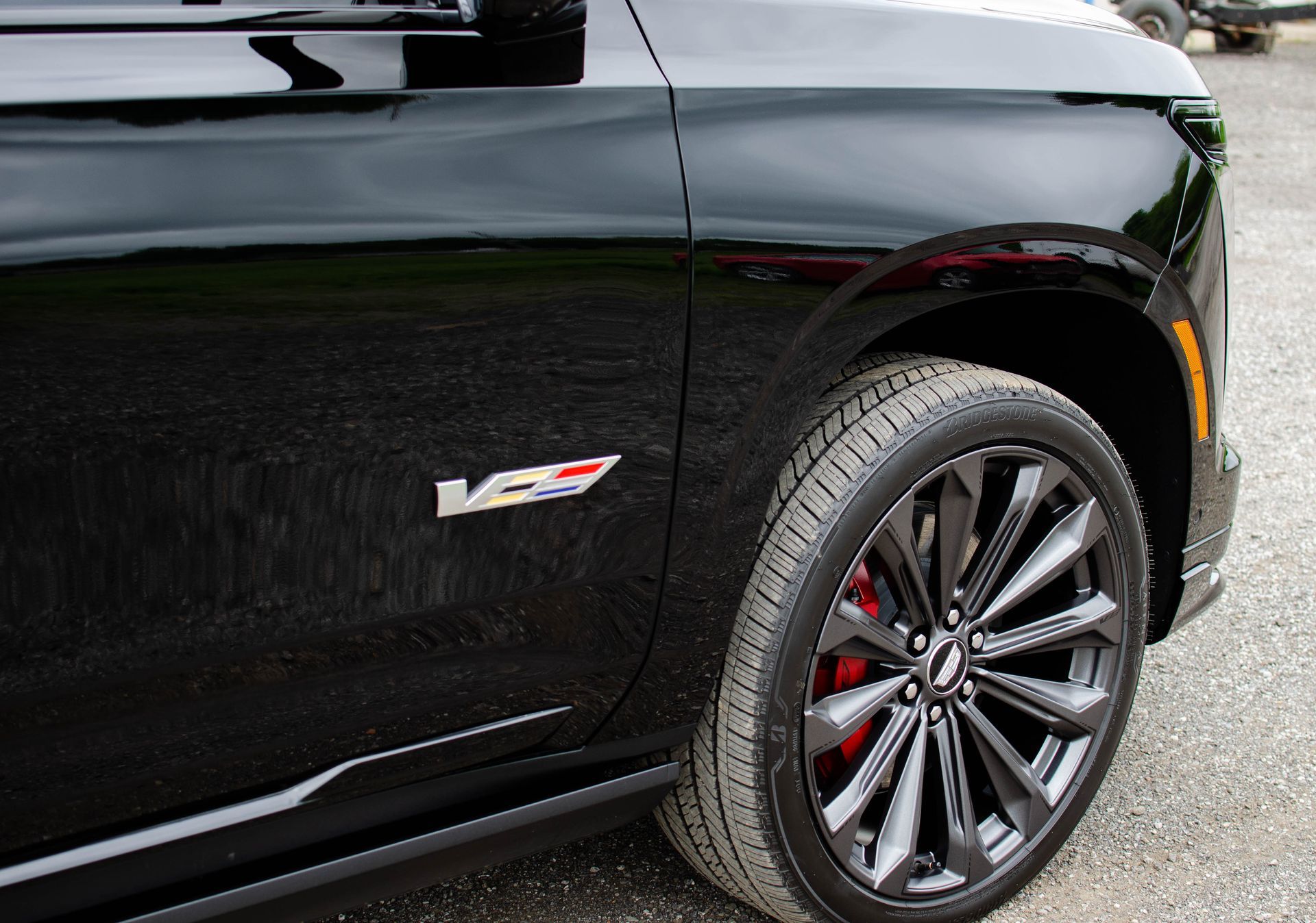 Black Cadillac SUV side view with V badge, showing front wheel and red brake caliper.