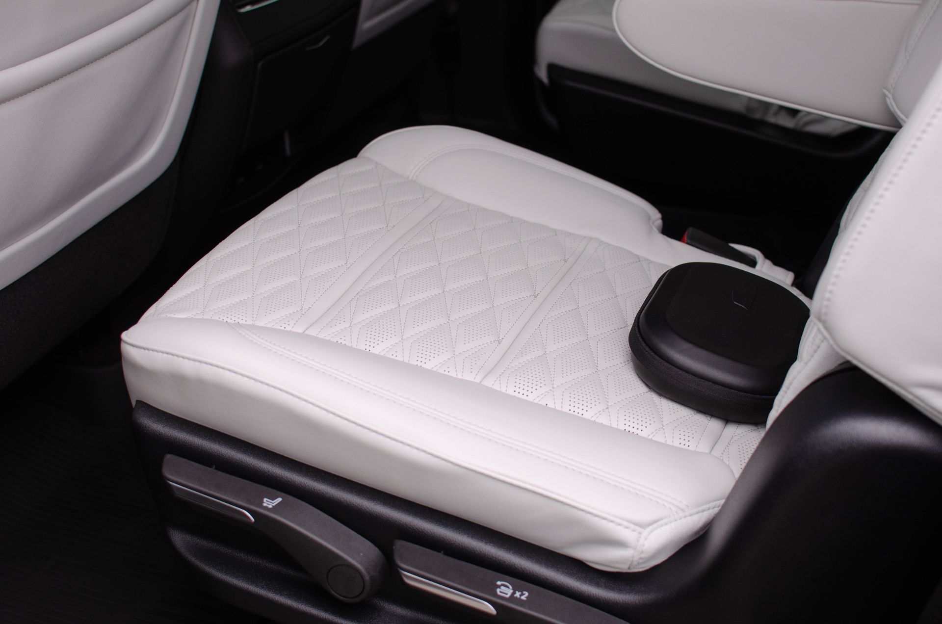 White leather car seat with quilted center and a small black bag on the cushion