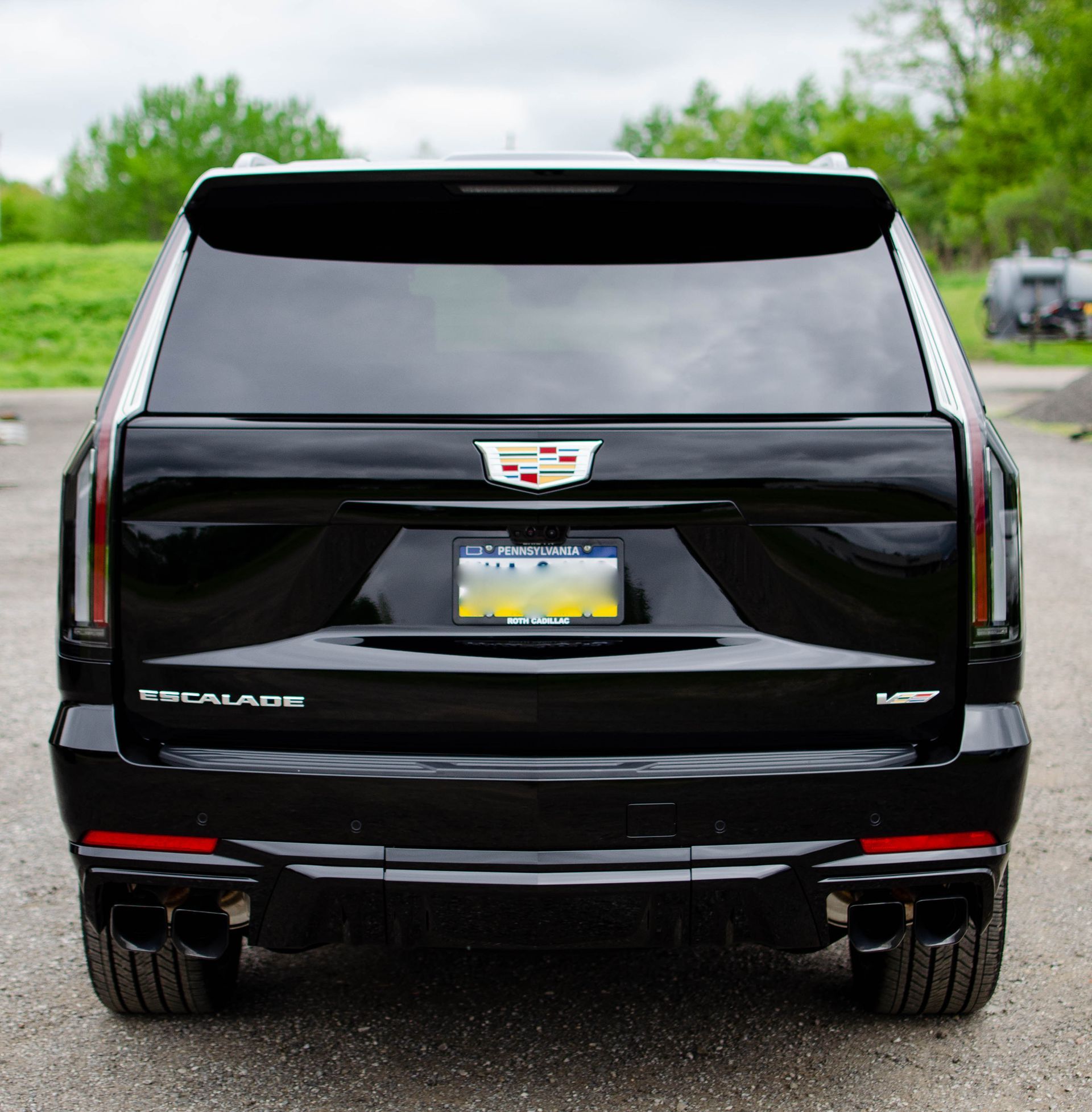 Rear view of a black Cadillac SUV parked on a road, with tinted windows and a visible license plate.