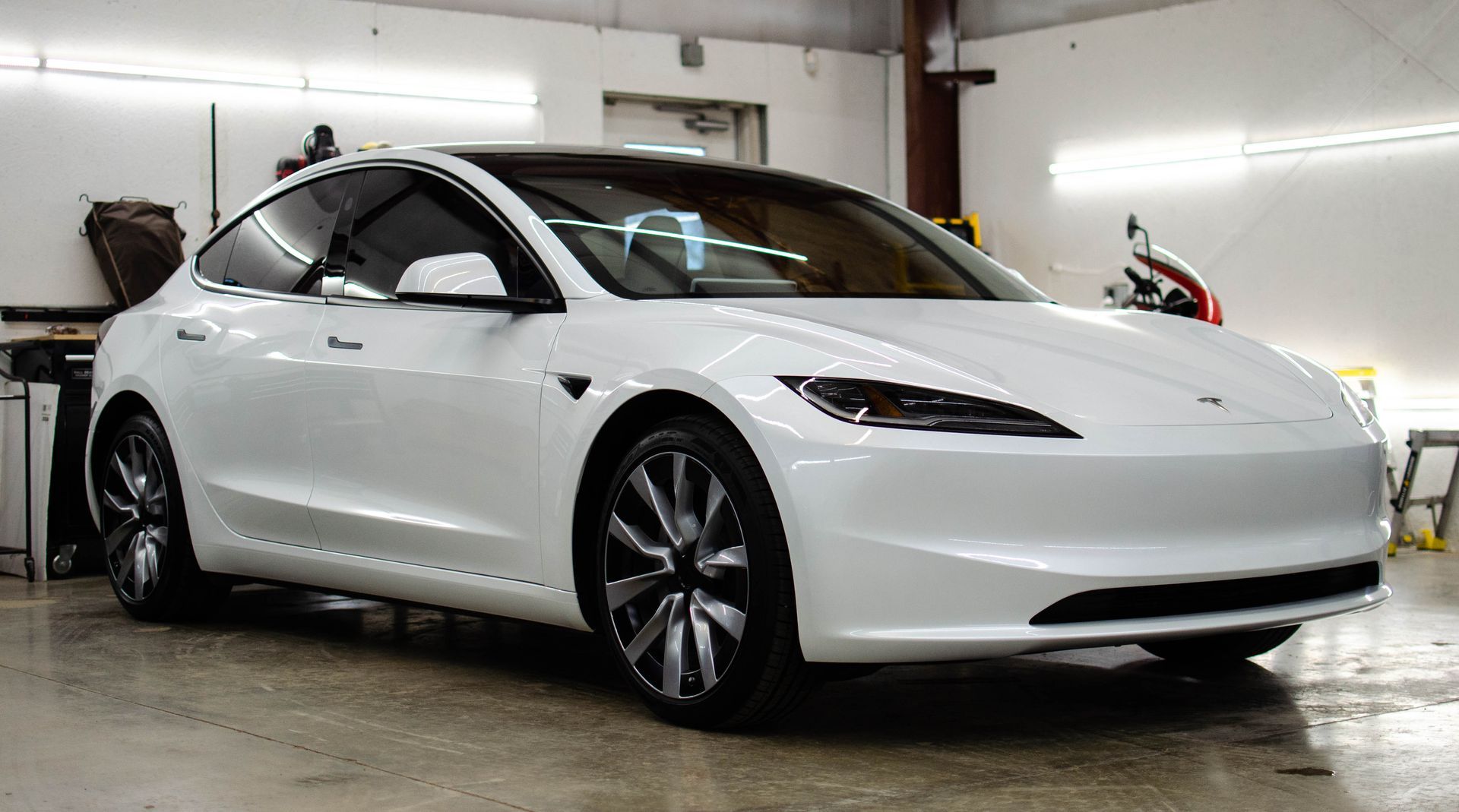 White Tesla sedan parked indoors in a garage, viewed from the front-left side.