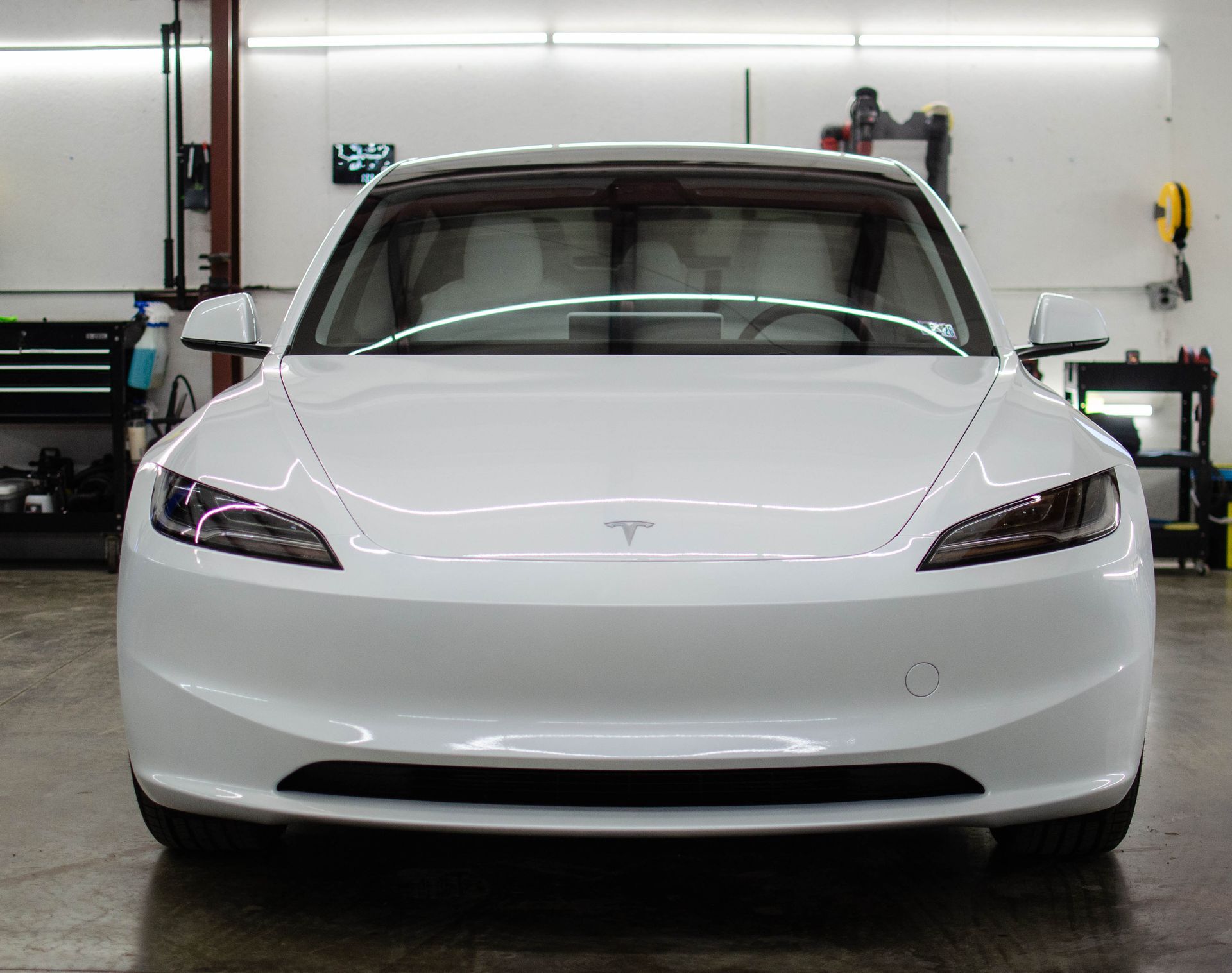 Front view of a white Tesla sedan in a garage with workshop equipment in the background