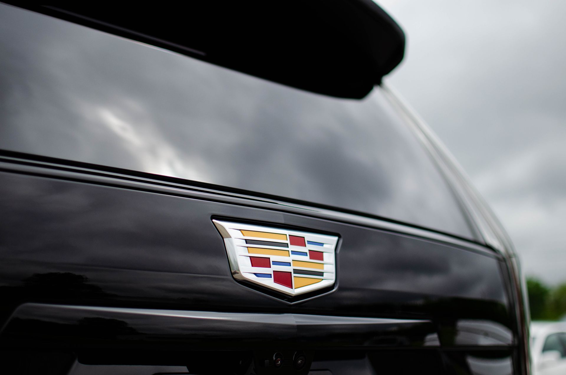 Close-up of a black Cadillac hood with the gold-and-red crest emblem against a cloudy sky