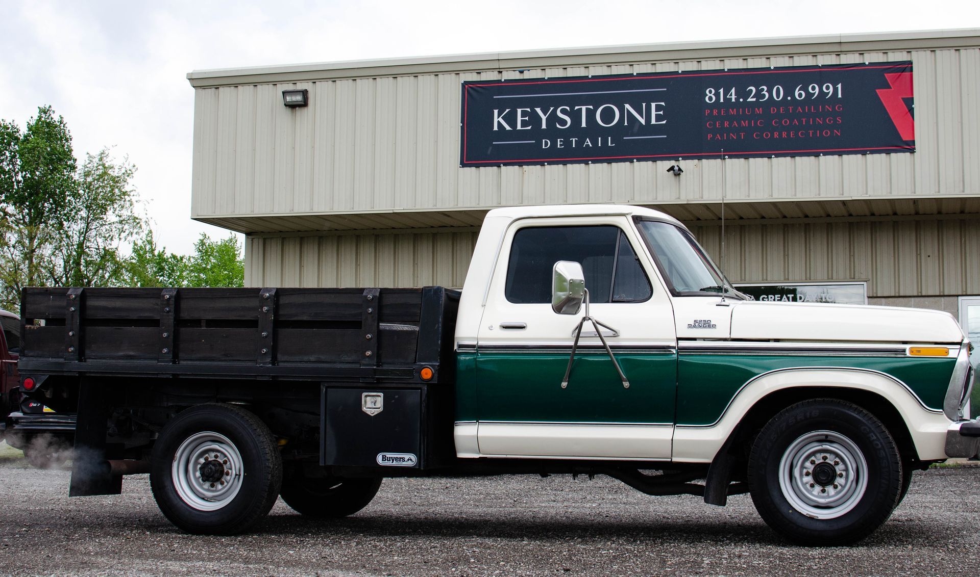 White-and-green flatbed truck parked beside a building with a Keystone sign.