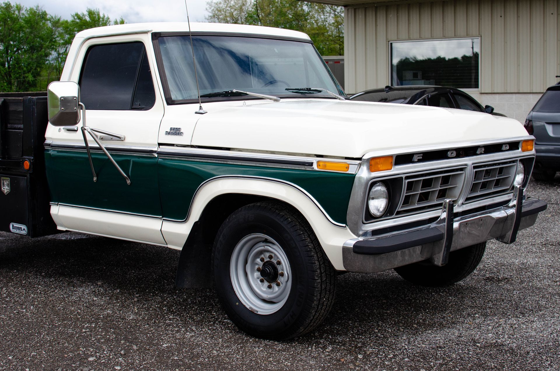 White and green vintage SUV parked outdoors on gravel near a building