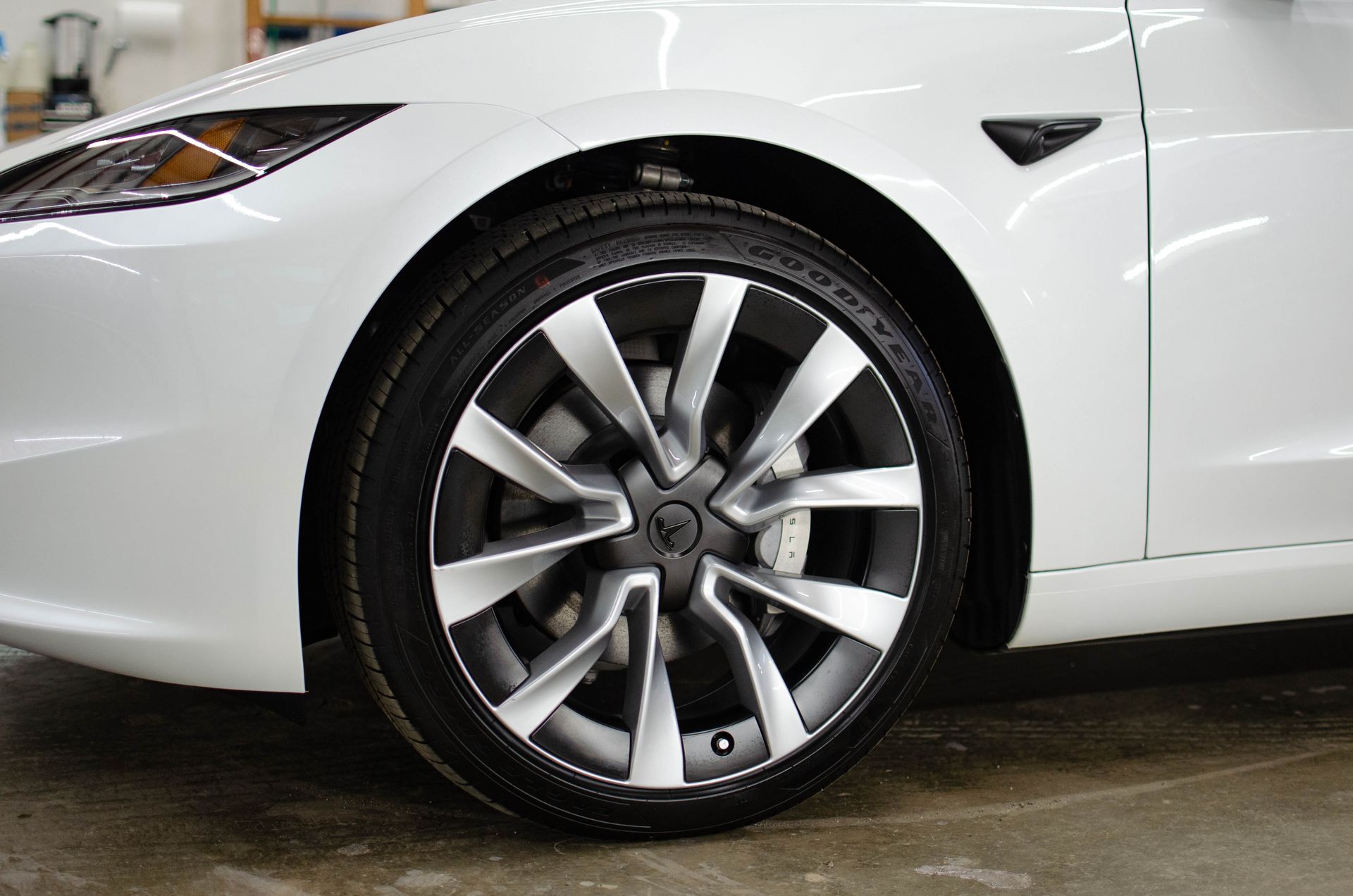 Close-up of a white car’s front wheel and fender with a silver alloy rim.