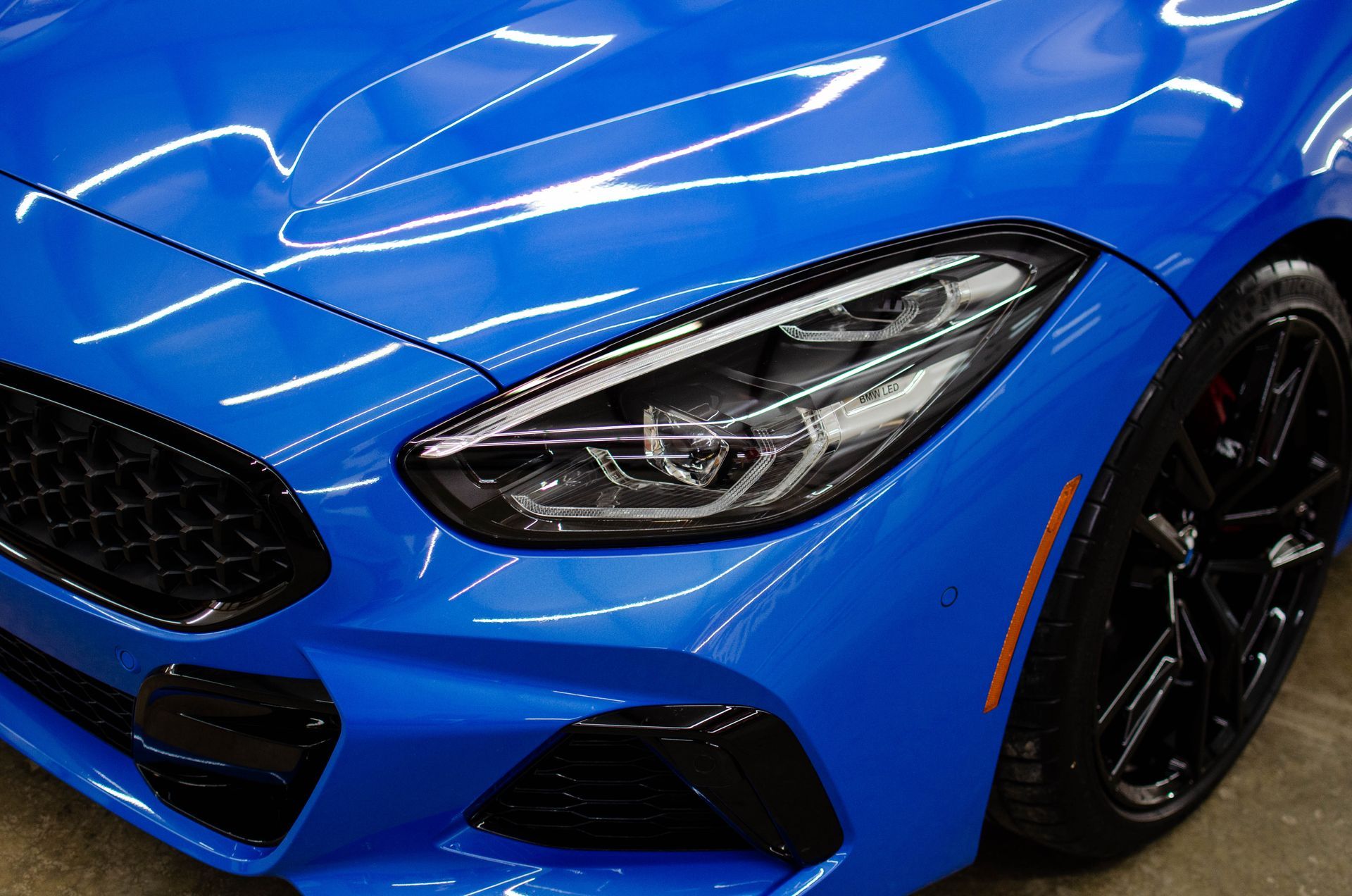 Close-up of a blue sports car front end with black grille and wheel
