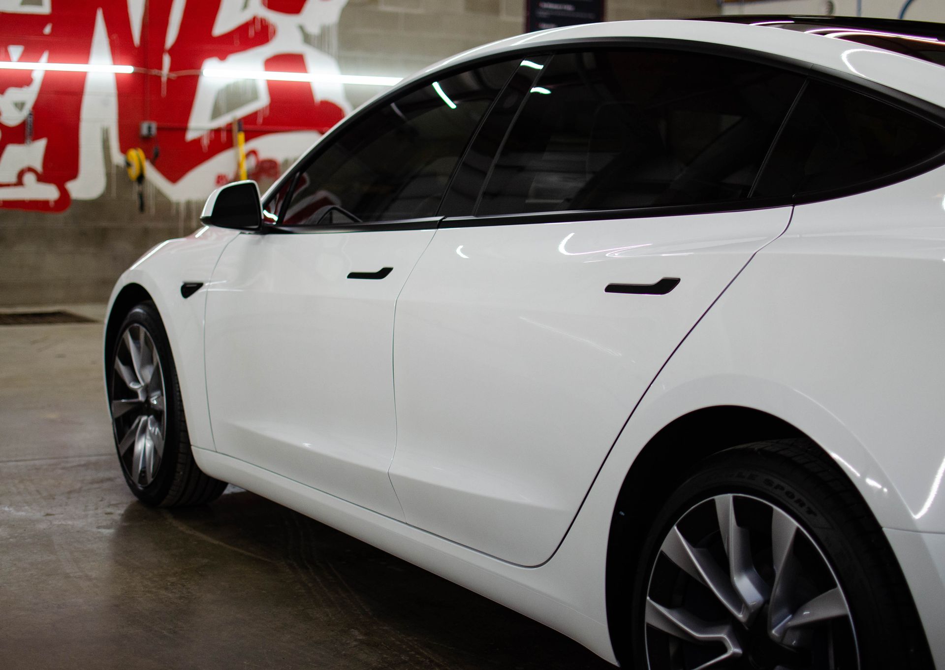 White sedan parked indoors beside a red graffiti wall