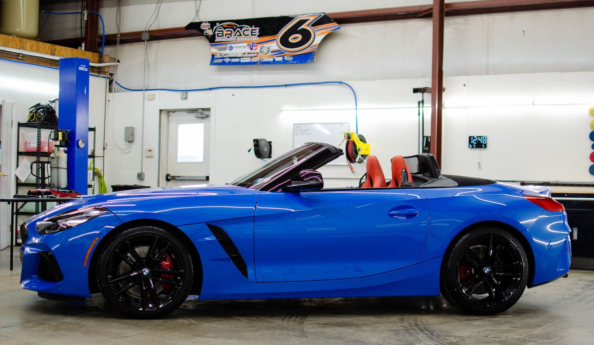 Blue convertible sports car in a garage, shown in side view with the top down.