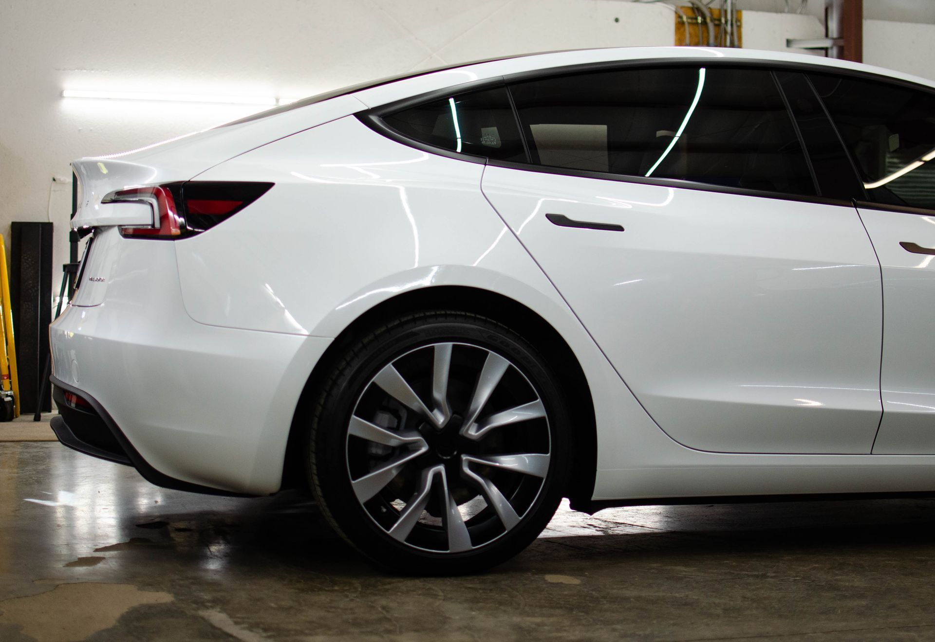 Rear side view of a white sedan parked indoors on a wet floor