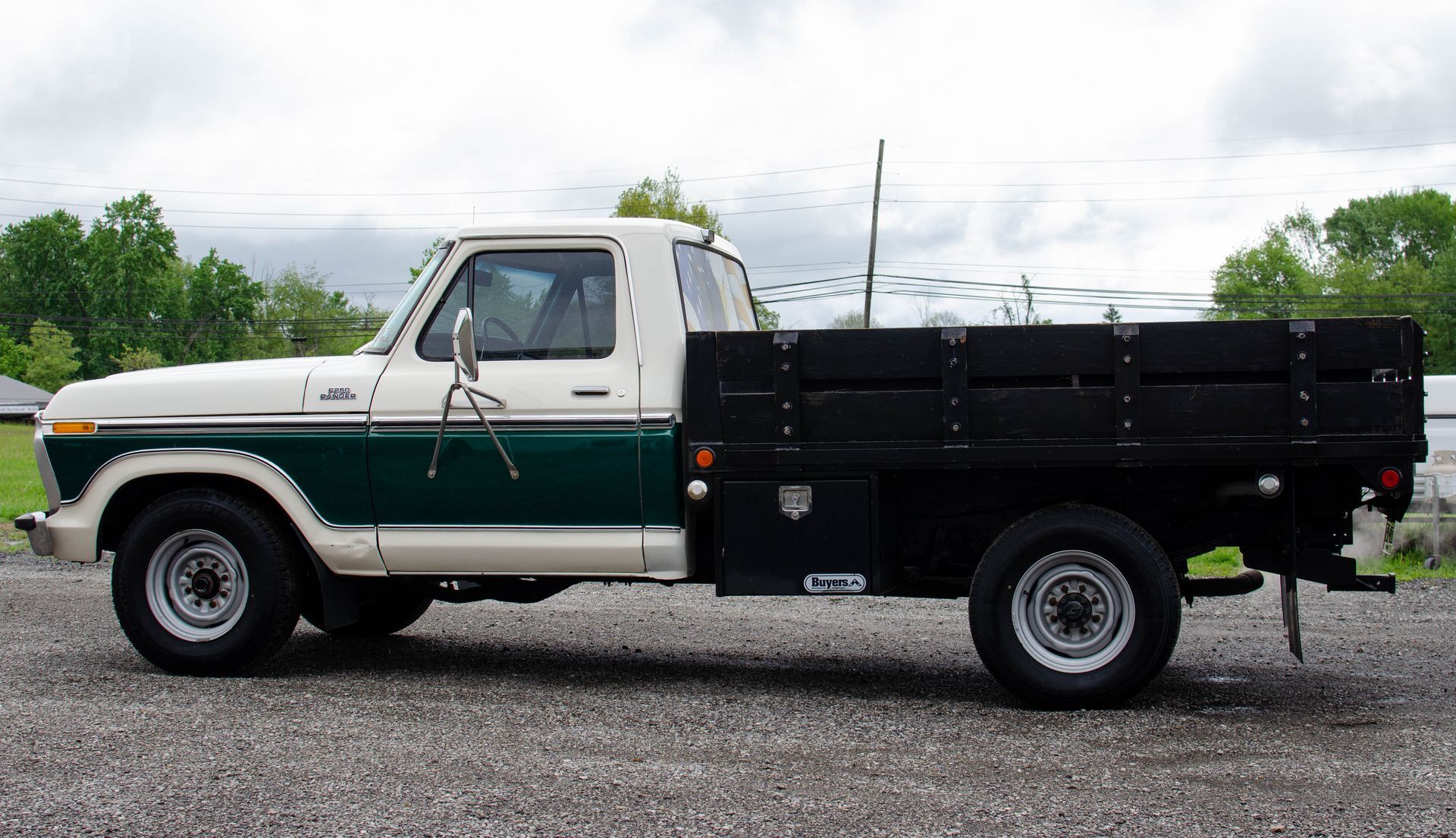 White and green pickup truck with a black flatbed, parked on gravel outdoors
