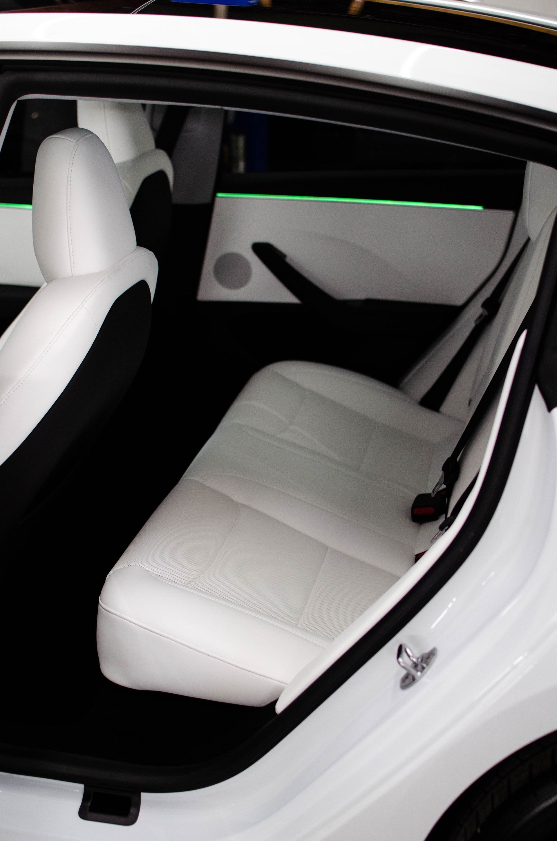 White car interior with rear seat folded down, showing a white upholstered back seat and open door.