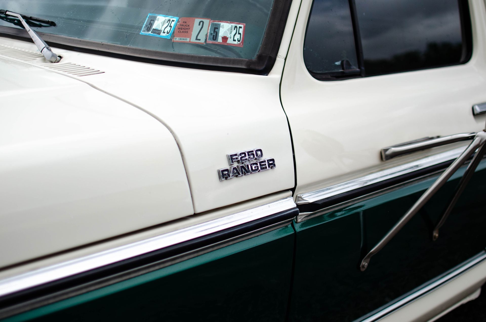 Close-up of a white vintage car door with chrome trim and badge against a dark green body panel