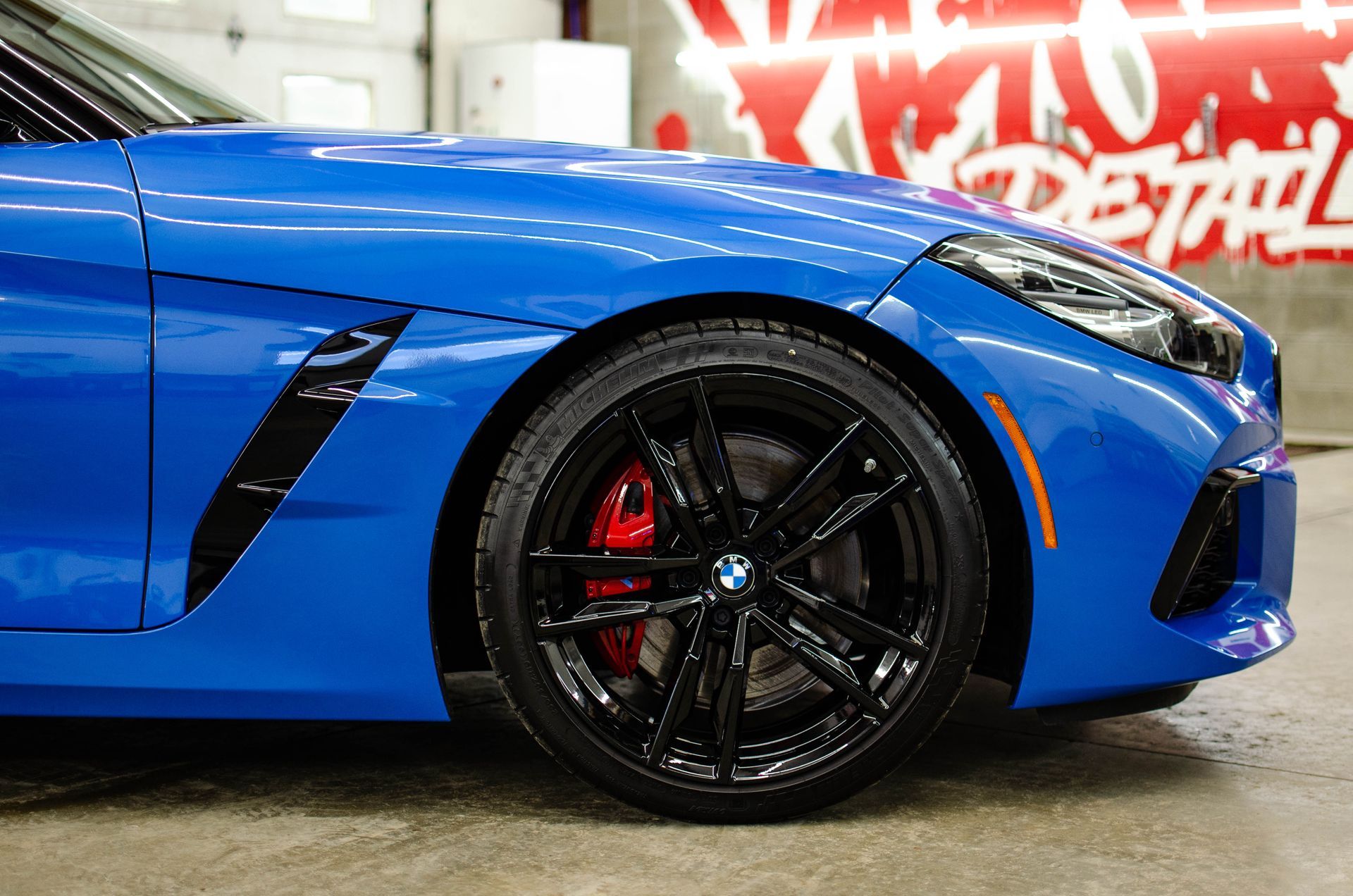 Blue sports car side view with black rims and red brake calipers in a garage.