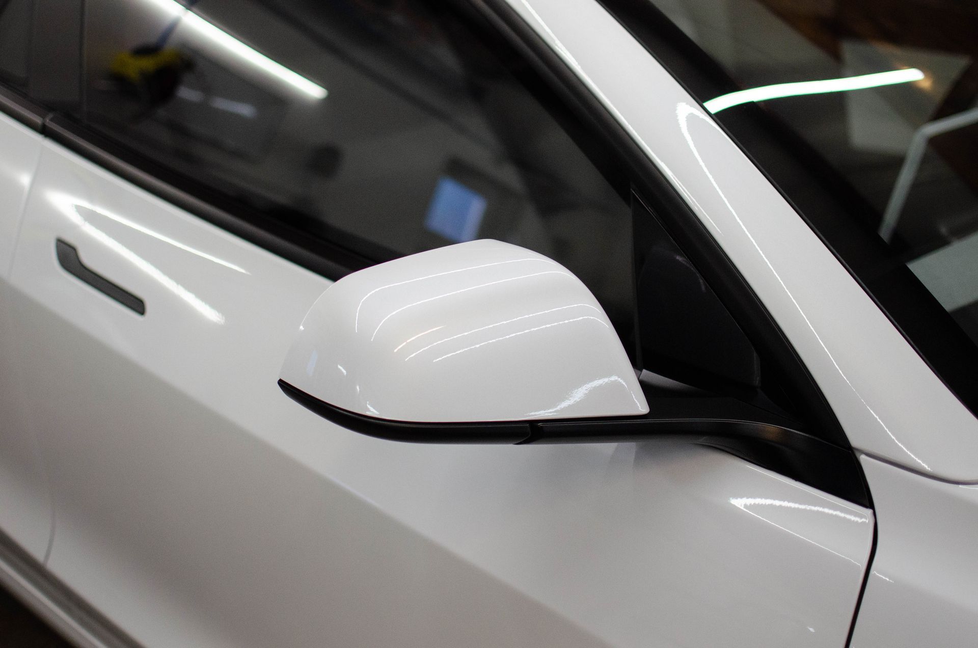 White car side mirror close-up with black trim and glossy reflections