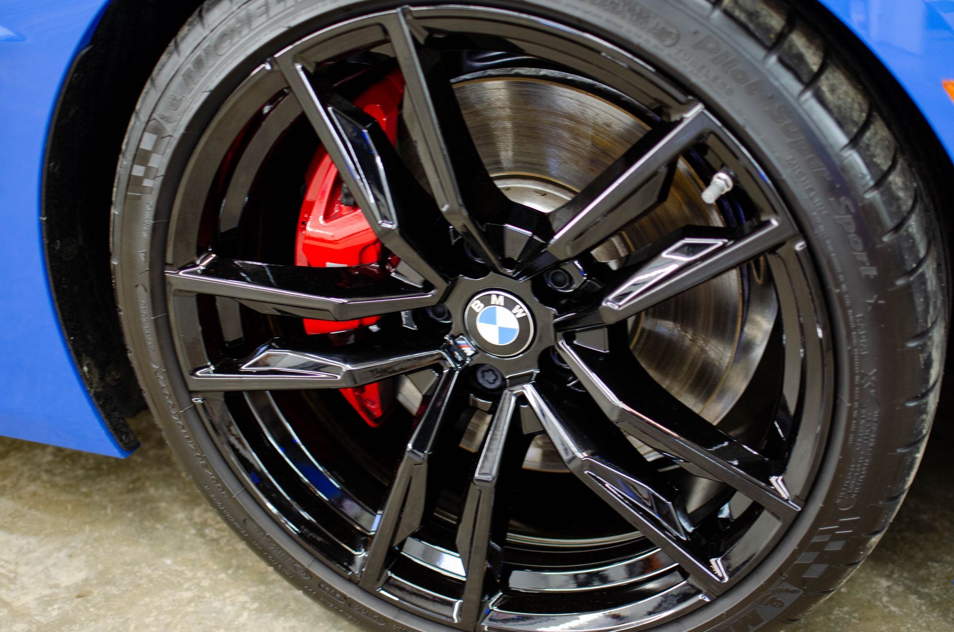 Close-up of a BMW black alloy wheel with red brake caliper on a blue car