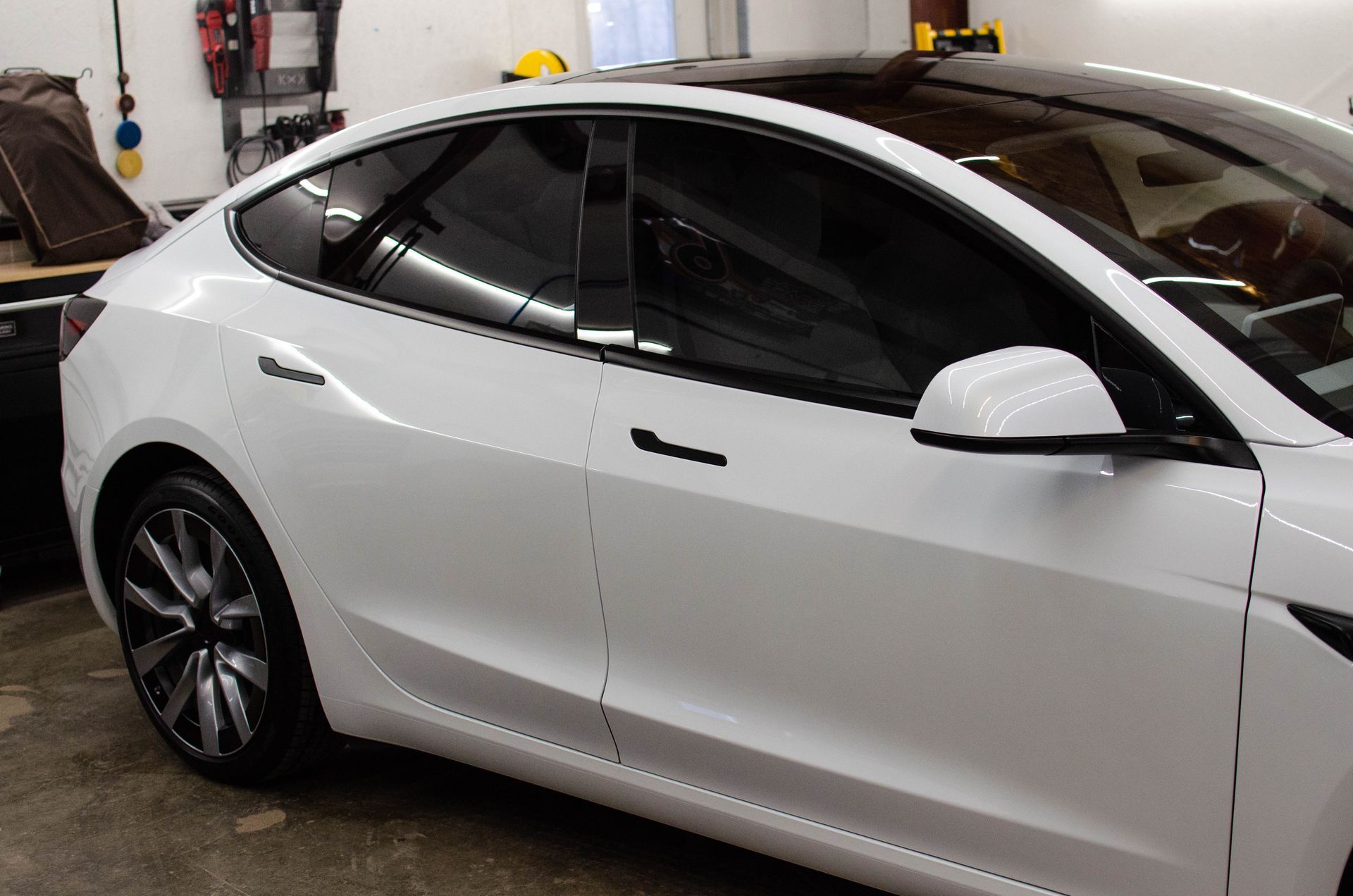 White Tesla sedan parked in a garage, side view with tinted windows and black rims