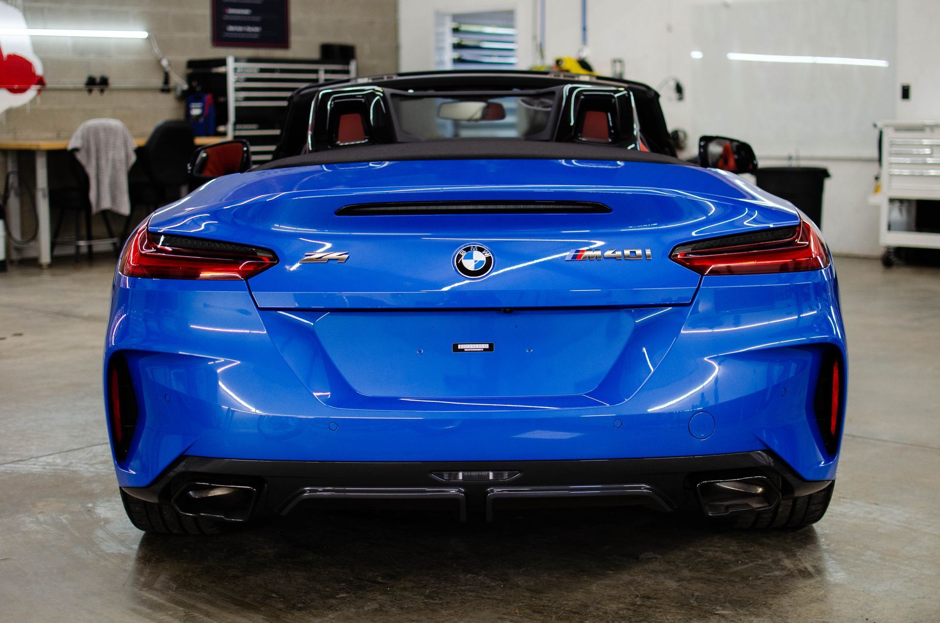 Rear view of a blue BMW convertible in a showroom, with people and cars in the background