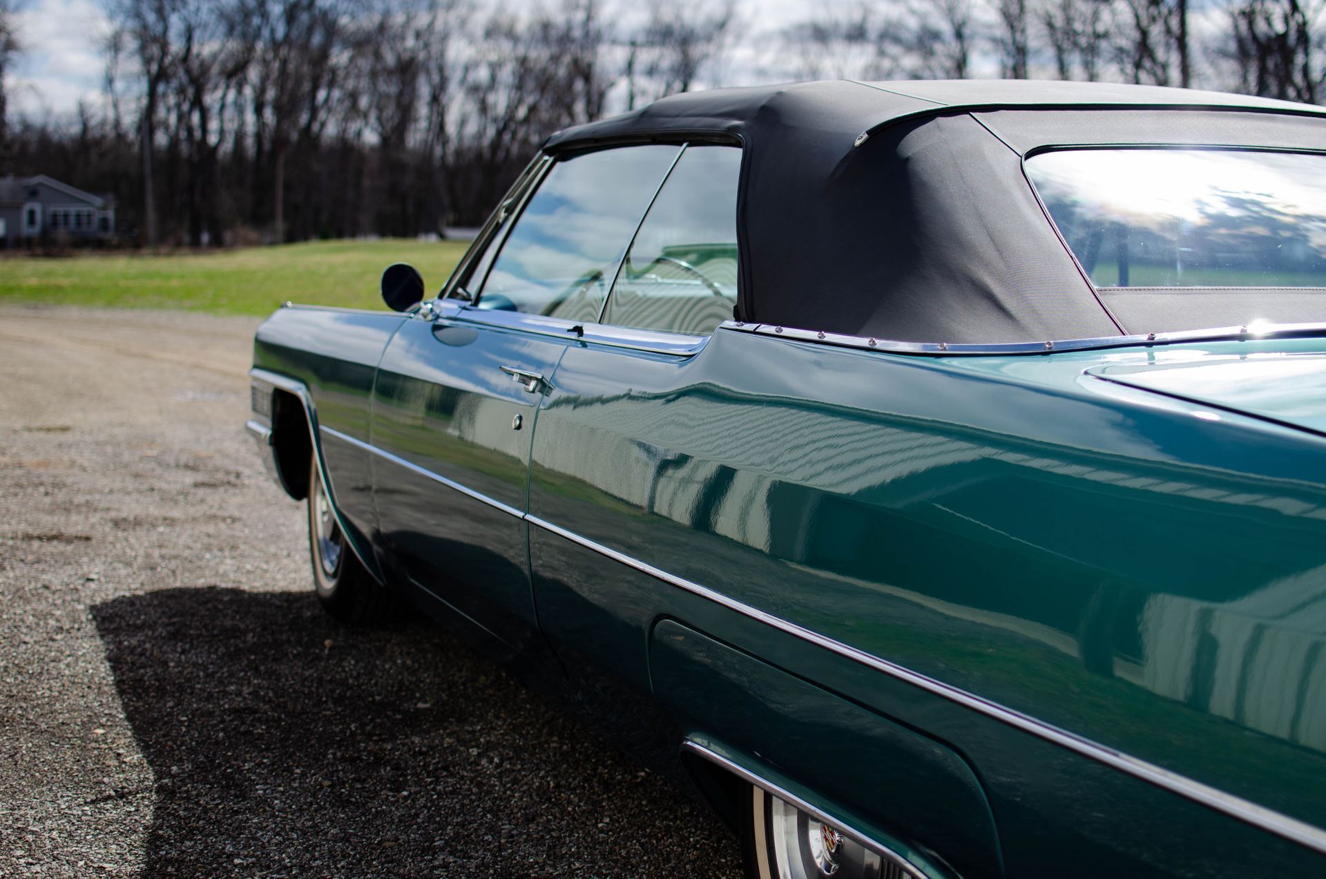 Green classic convertible car with black soft top parked on a gravel lot outdoors