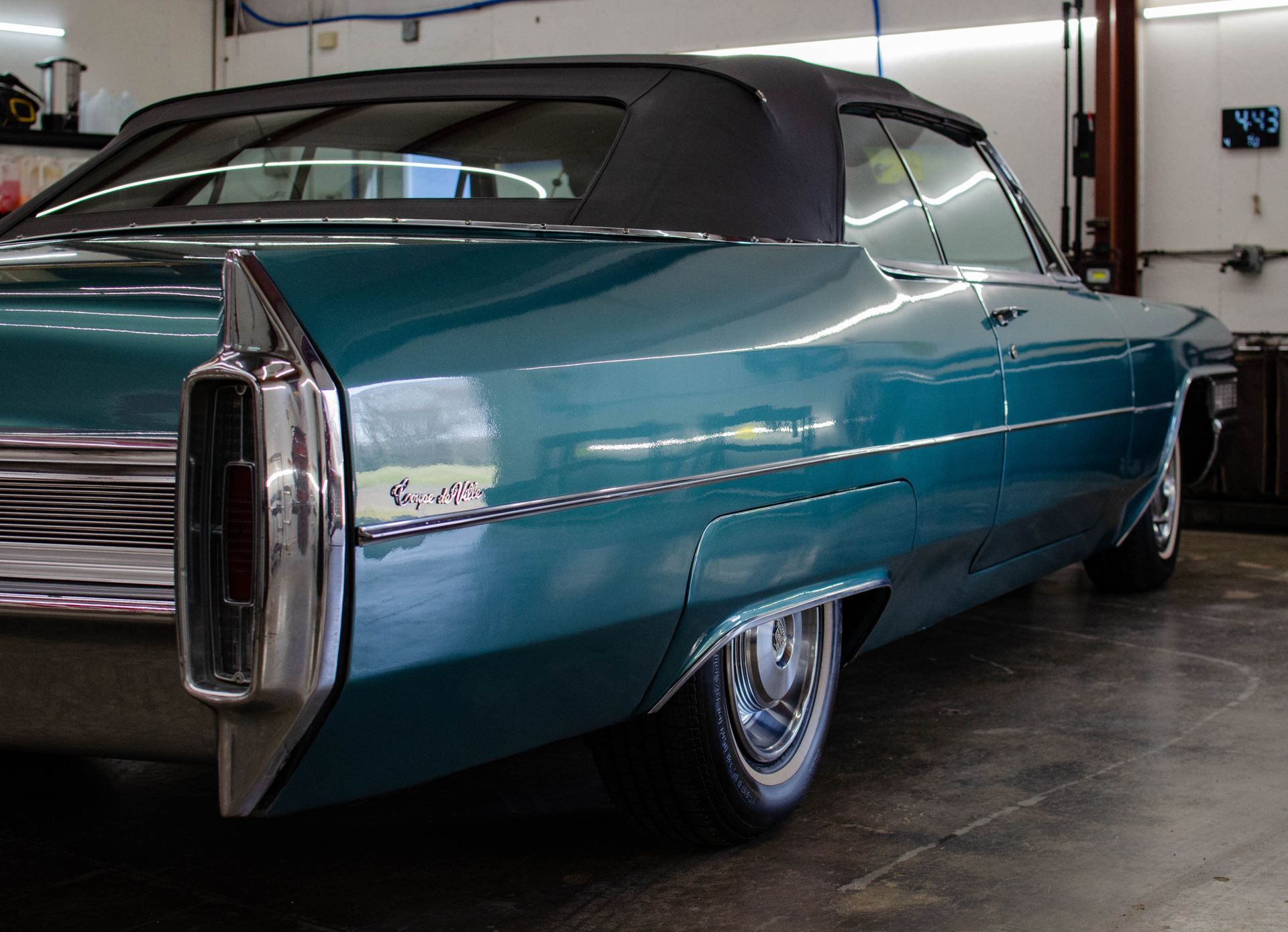 Turquoise classic car parked in a garage, rear side view with chrome fins and black vinyl top