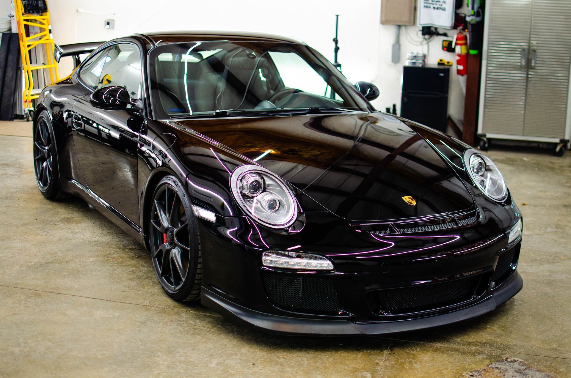 Black Porsche sports car parked in a garage, shown from the front-left angle