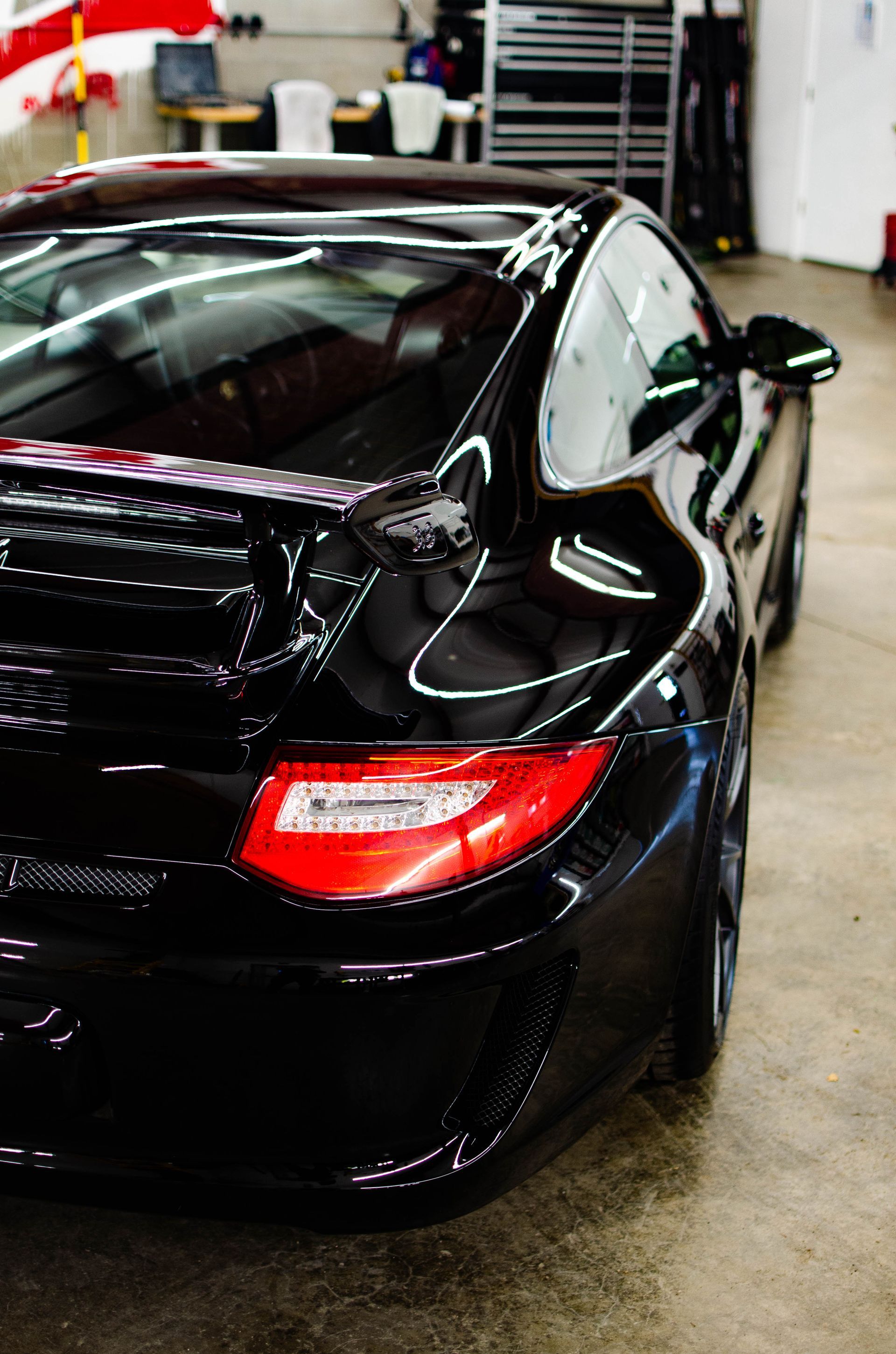 Black sports car parked in a garage, rear view with red taillights visible