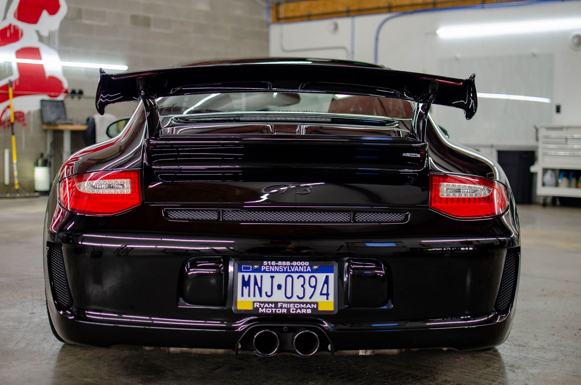 Rear view of a black sports car with a large spoiler and blue license plate in a garage
