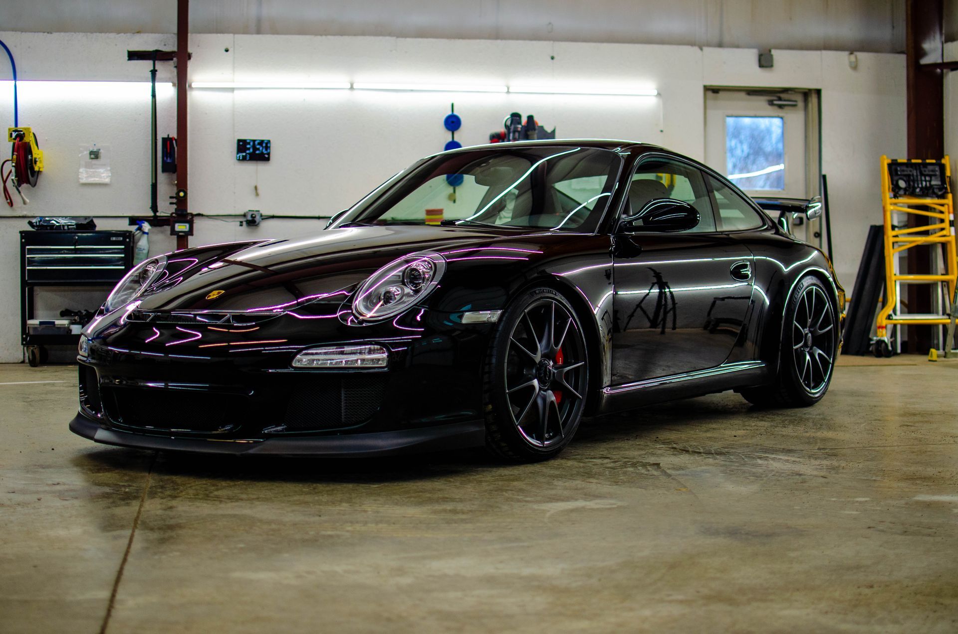 Black sports car parked in a garage, with purple-tinted headlights and black rims