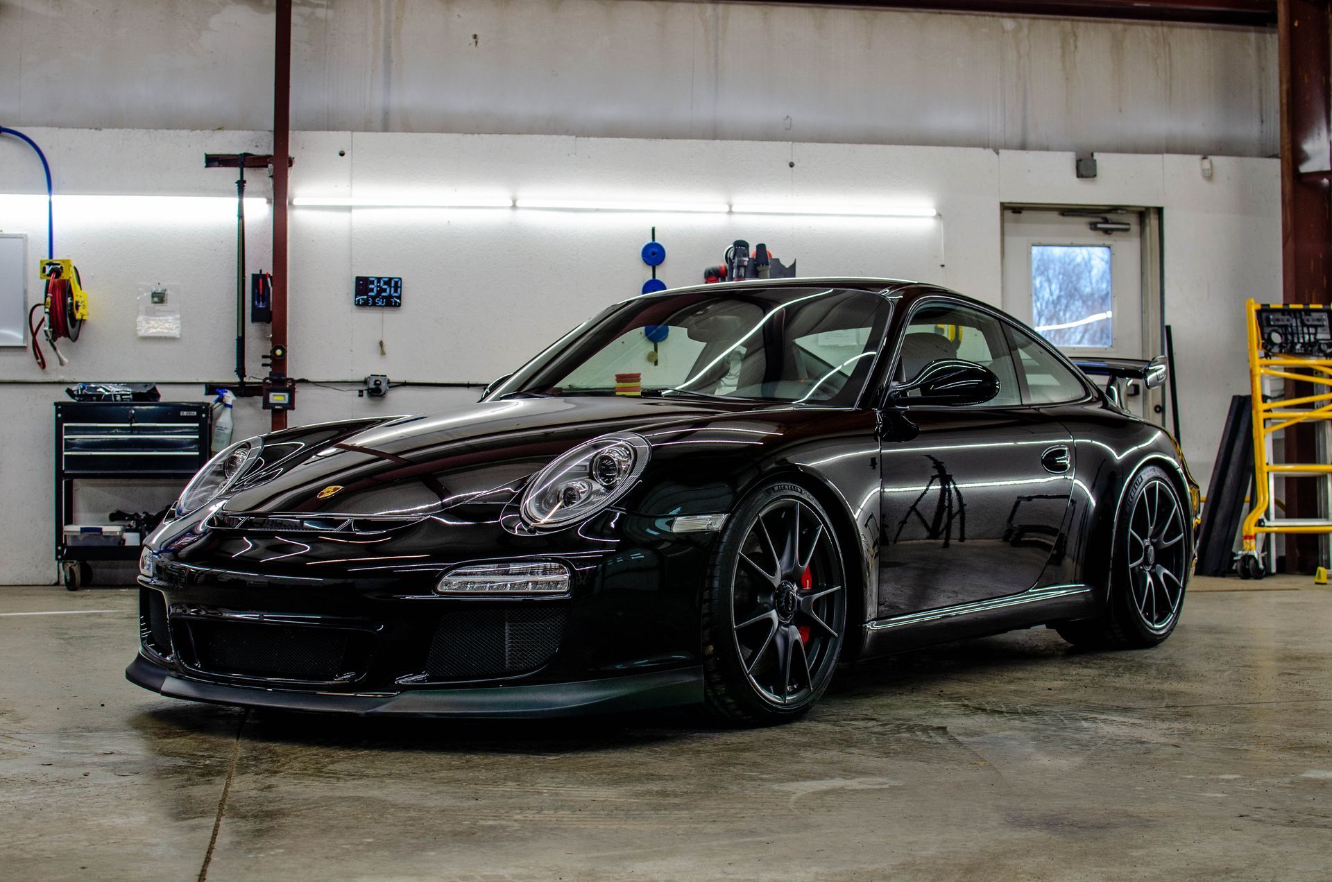 Black Porsche 911 sports car with racing accents parked inside a garage.