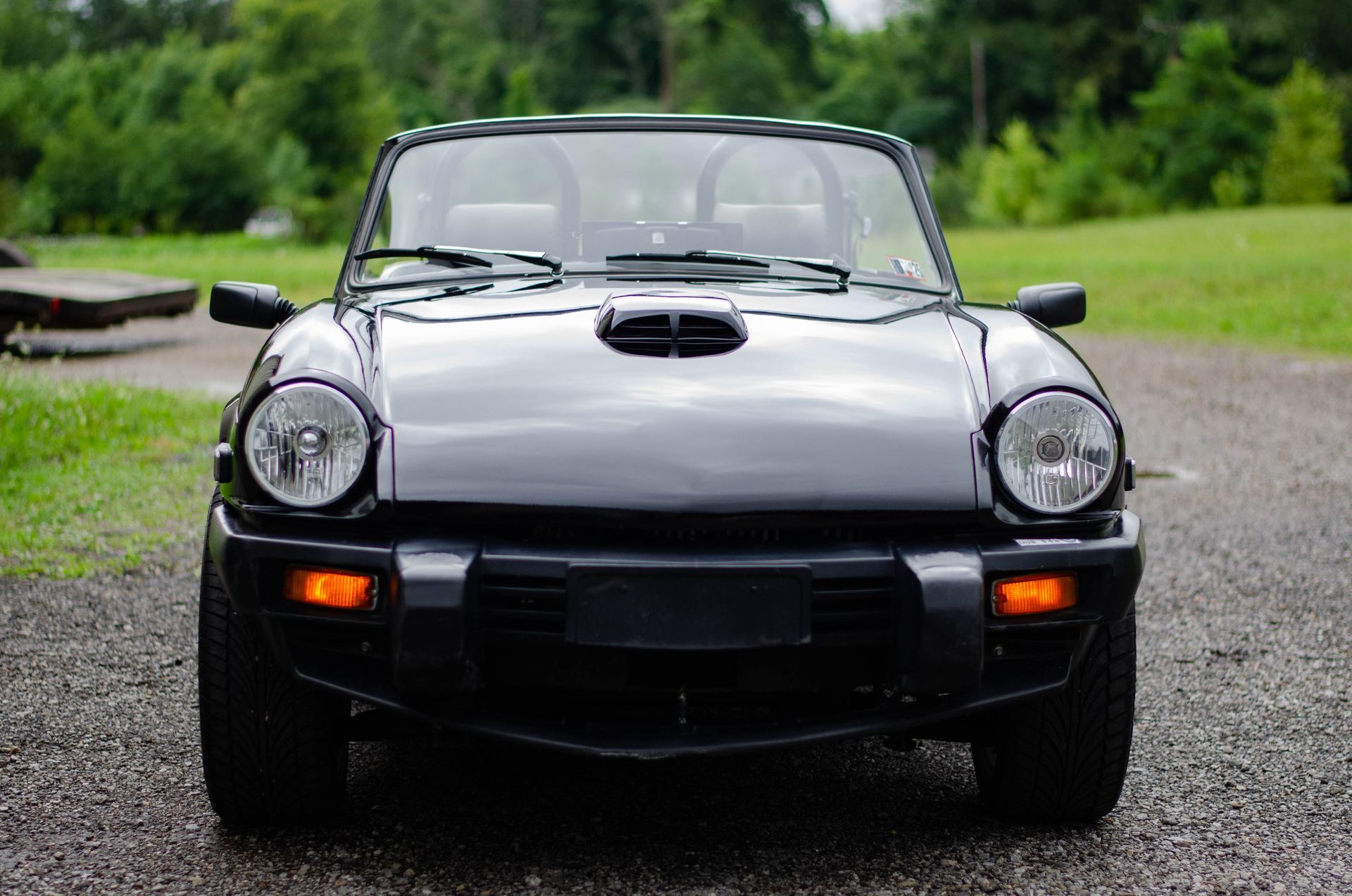 Front view of a black classic convertible sports car parked on wet pavement with trees in the background
