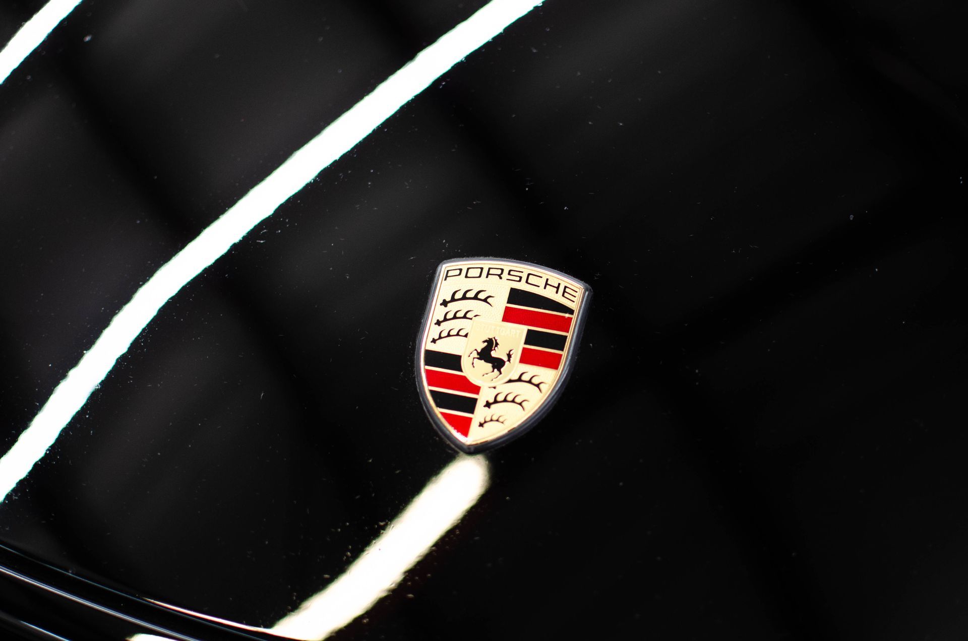 Porsche crest on a glossy black car hood with white reflections