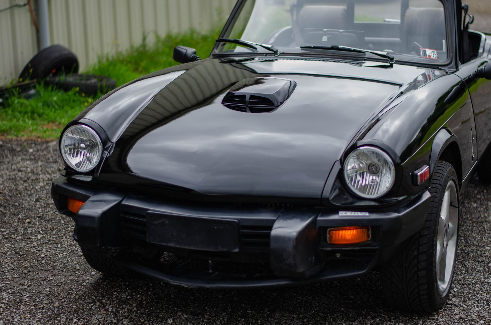 Black convertible sports car parked outdoors on gravel, front view