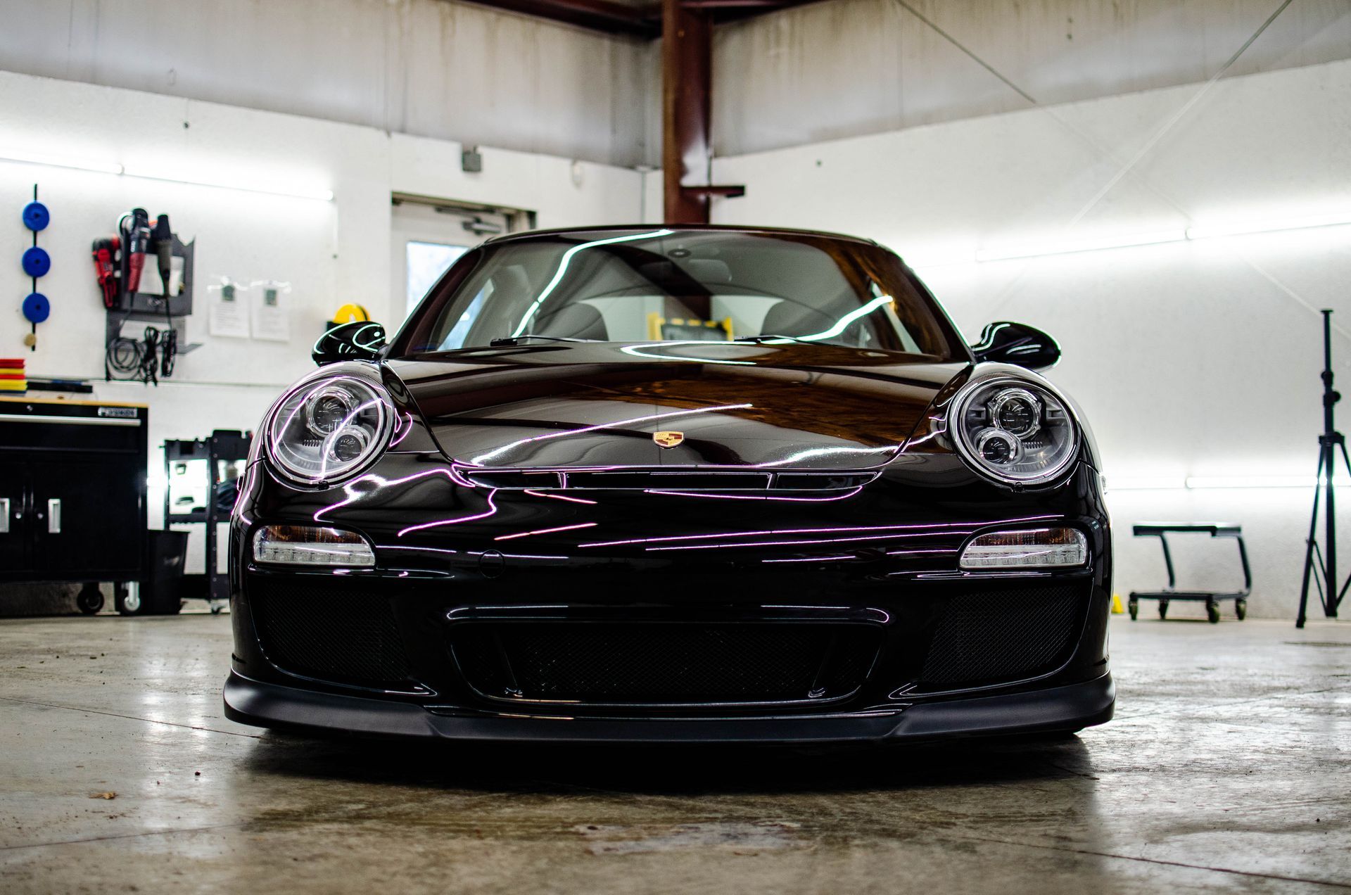 Front view of a low black sports car in a garage, with purple reflections on the hood.