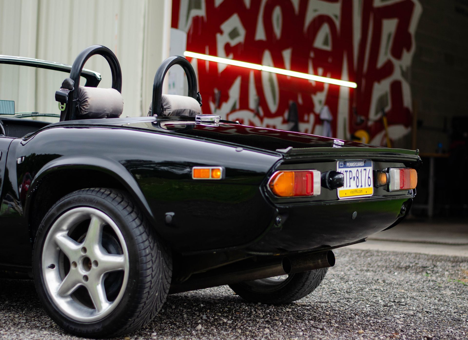 Black convertible sports car parked on gravel in front of a graffiti-covered wall