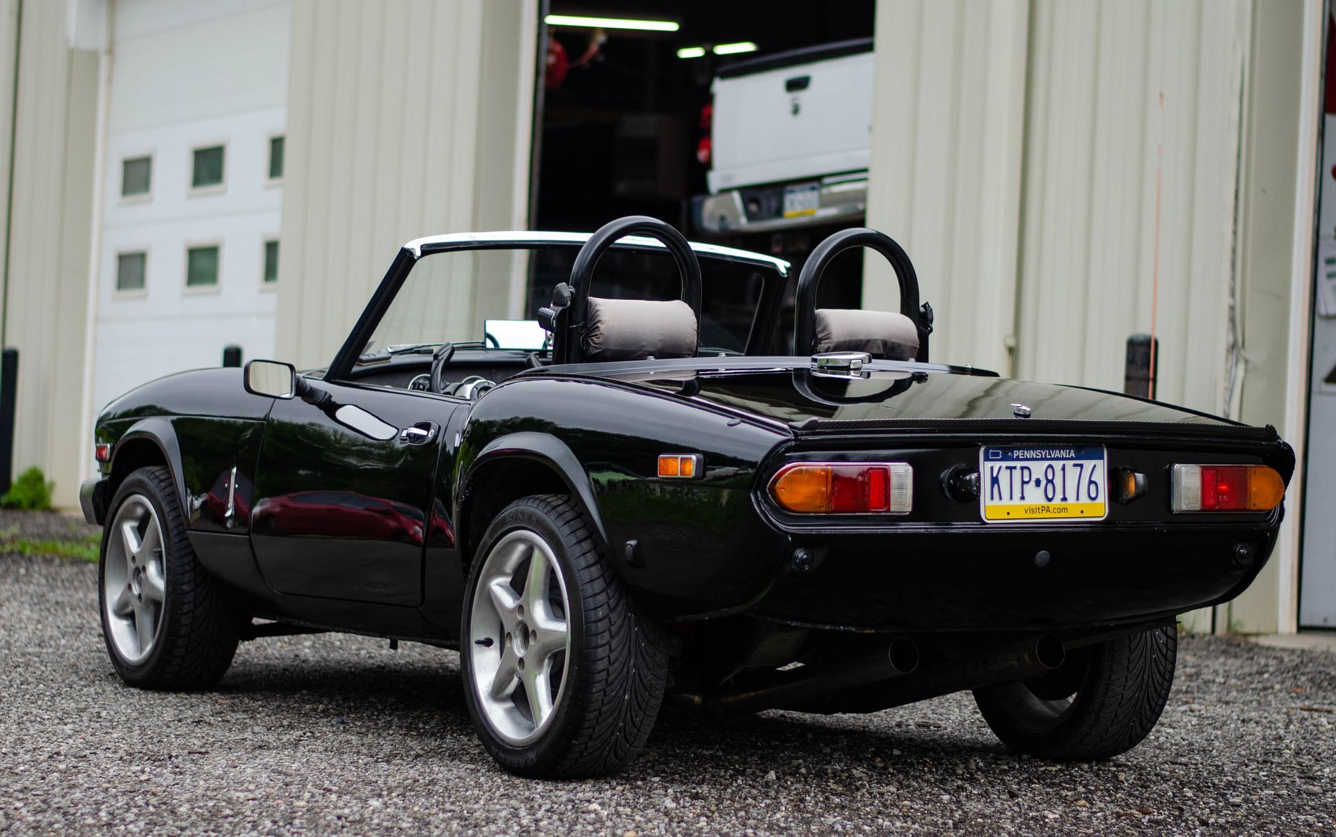 Black convertible sports car parked outside a garage, rear view with top down