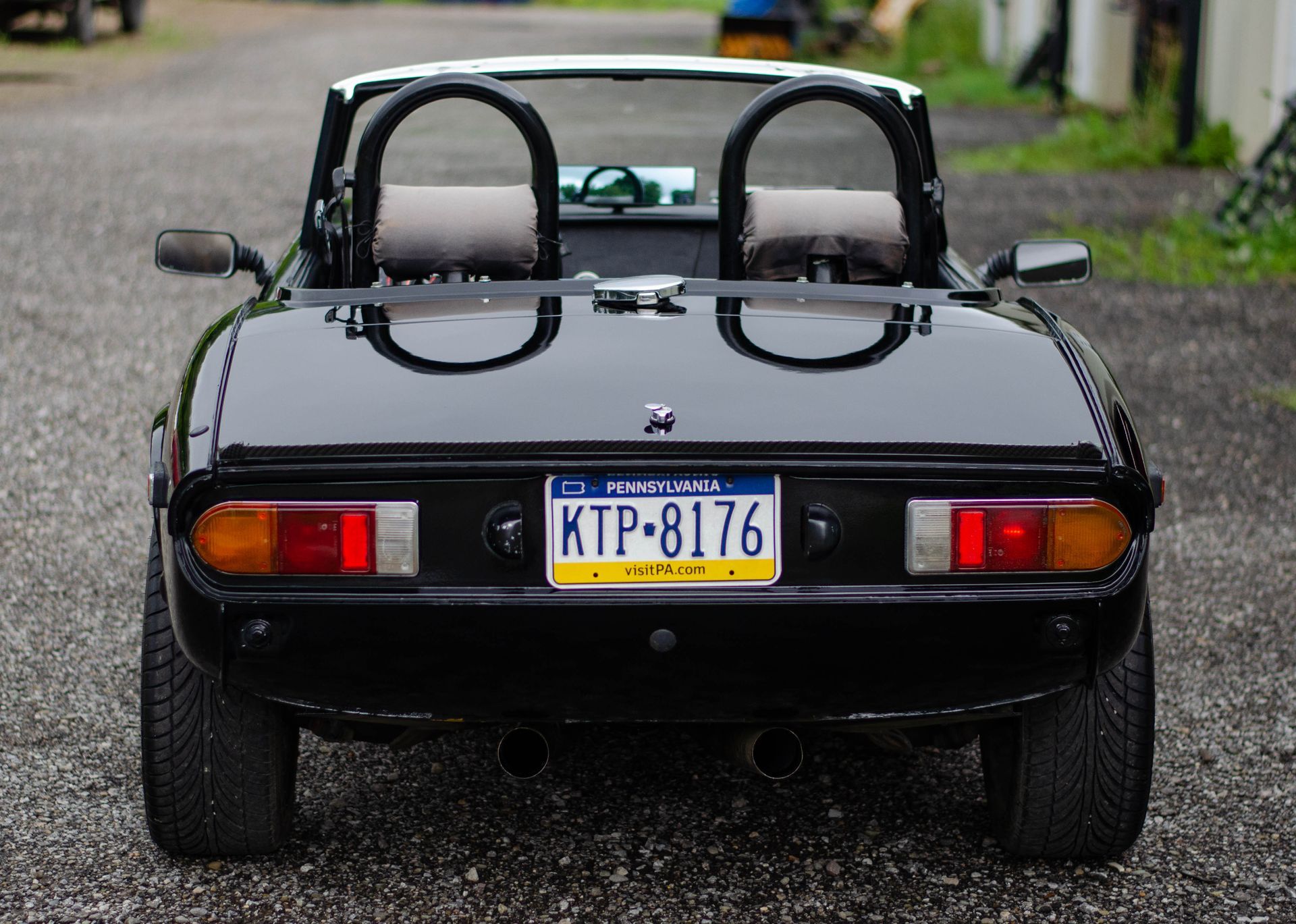 Rear view of a black convertible sports car with a New York license plate on a gravel road