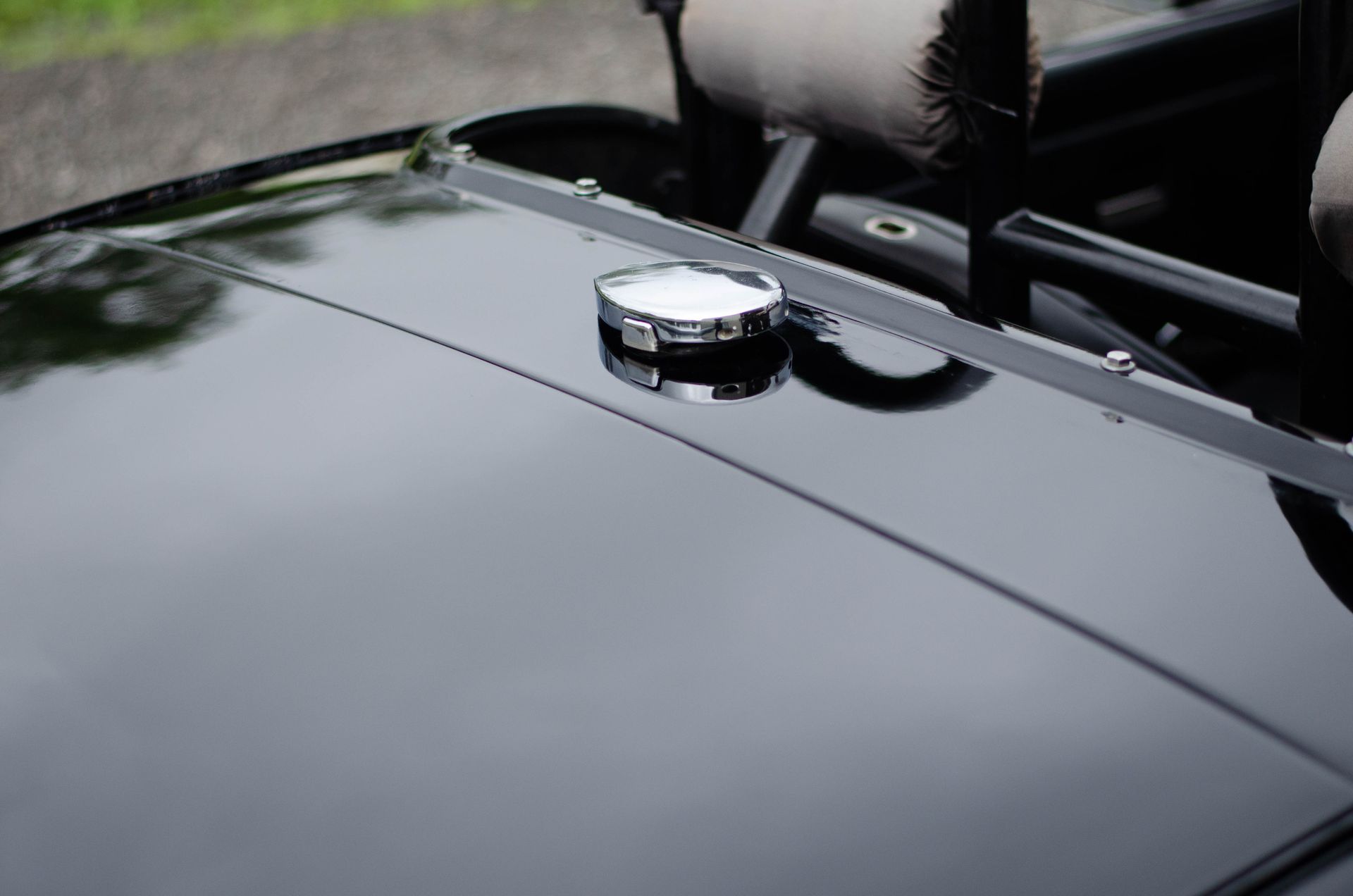 Close-up of a glossy black car hood with a chrome fuel cap and windshield reflection