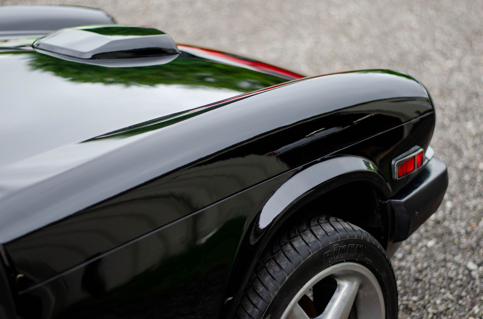 Close-up of a glossy black classic car’s front fender and hood scoop with red stripe detail.