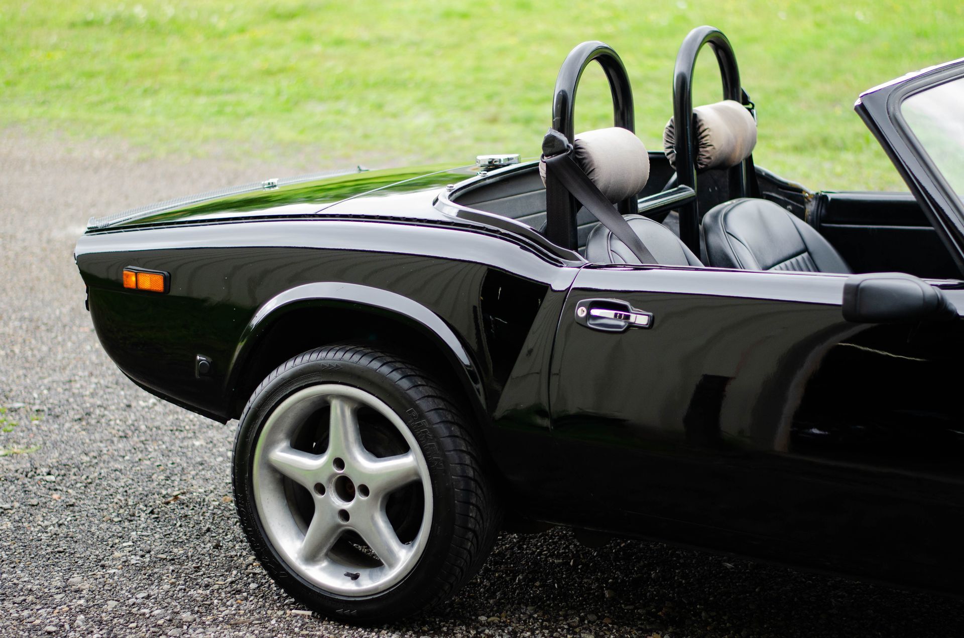 Black convertible sports car parked on gravel, side view with silver wheels and gray seats