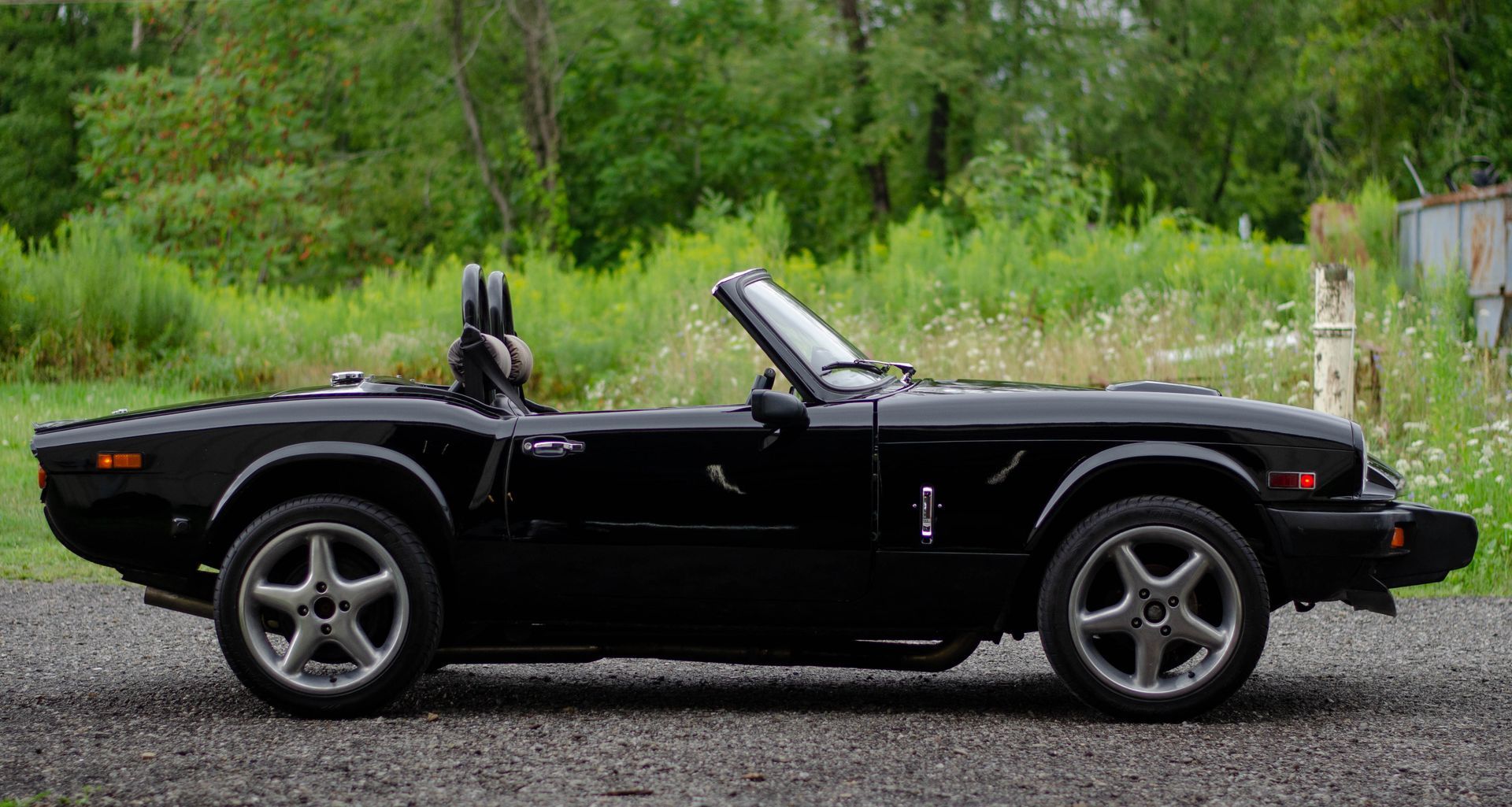 Black convertible sports car parked on gravel in front of green trees