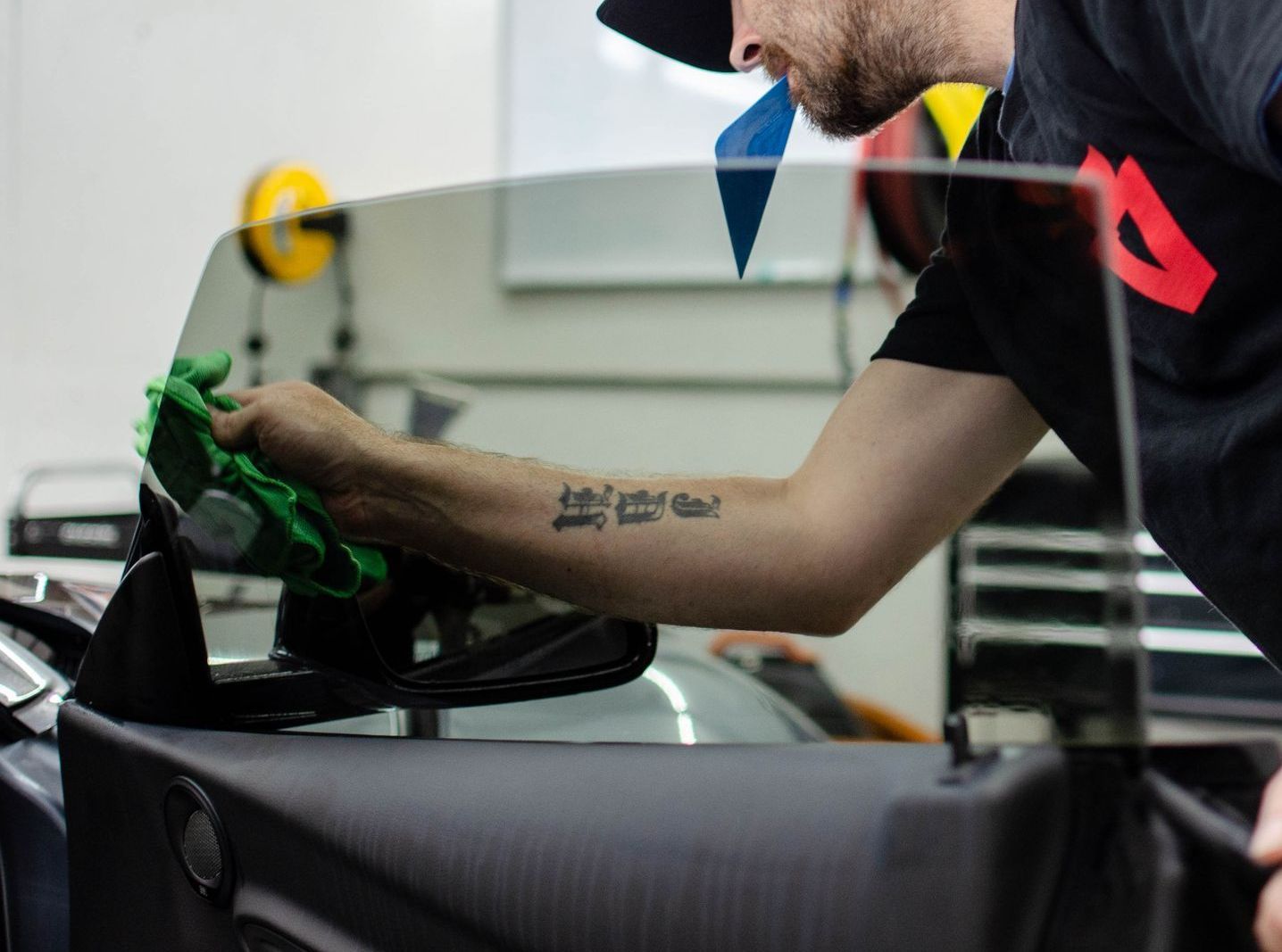 a man with a tattoo on his arm is cleaning the windshield of a car .