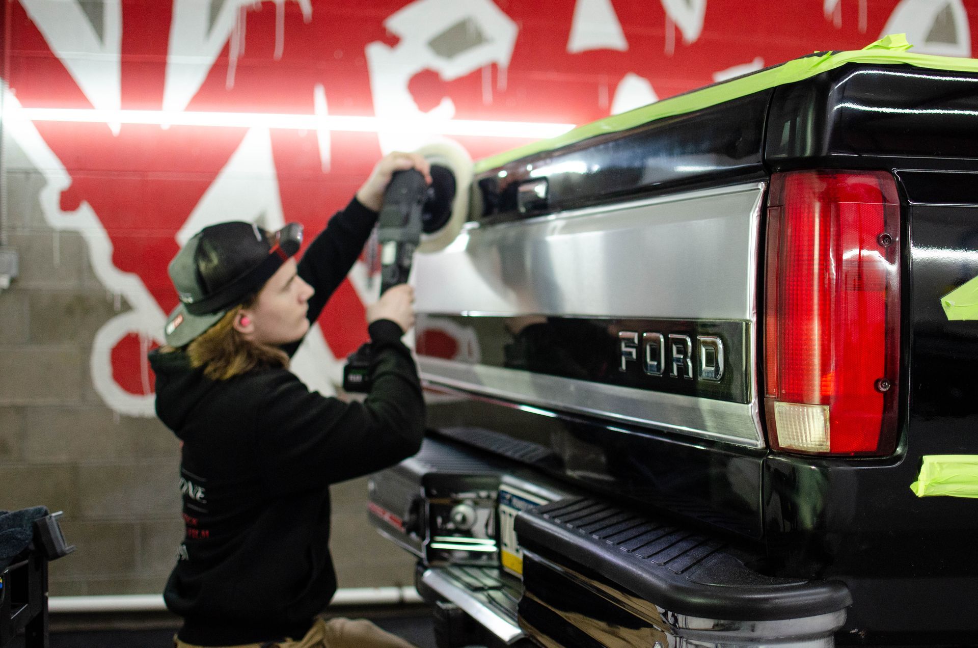 Person polishing the rear of a black Ford truck in a garage