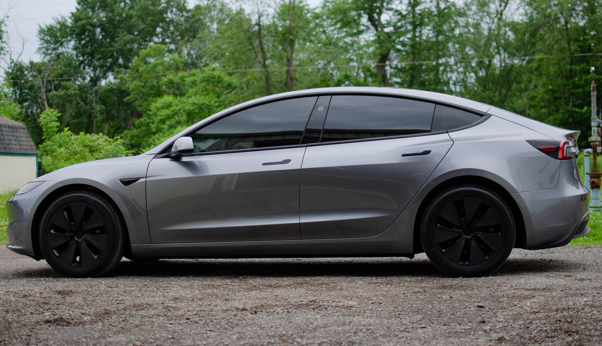 Gray Tesla sedan parked on gravel with trees in the background