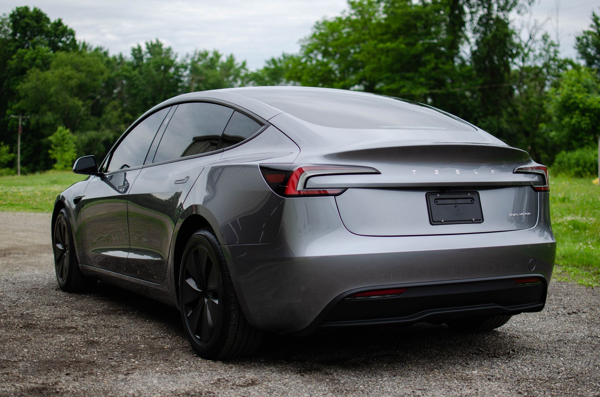 Silver sedan parked on gravel, rear three-quarter view with trees in the background