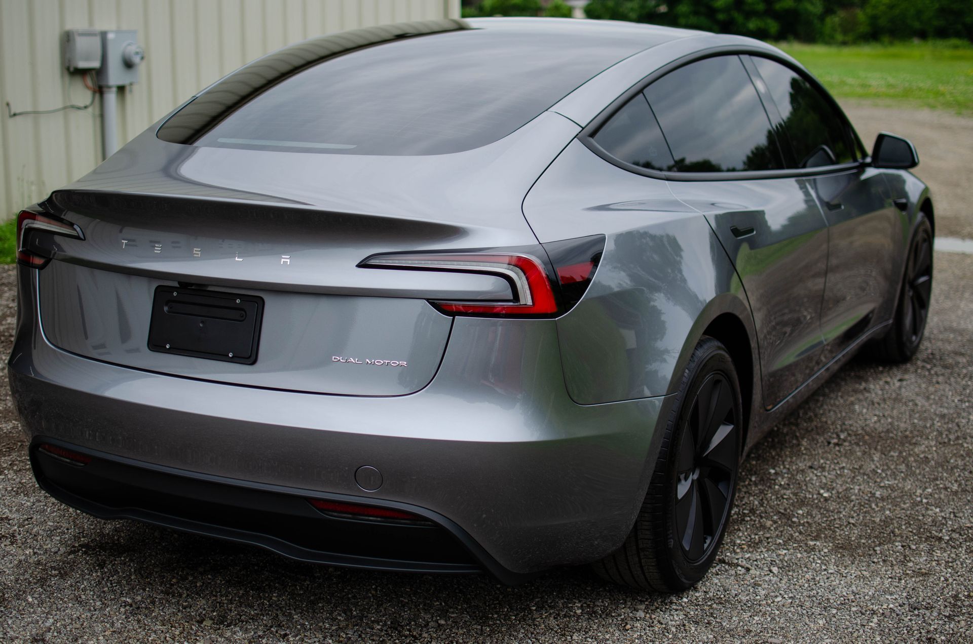 Silver Tesla sedan parked on a wet driveway, rear three-quarter view